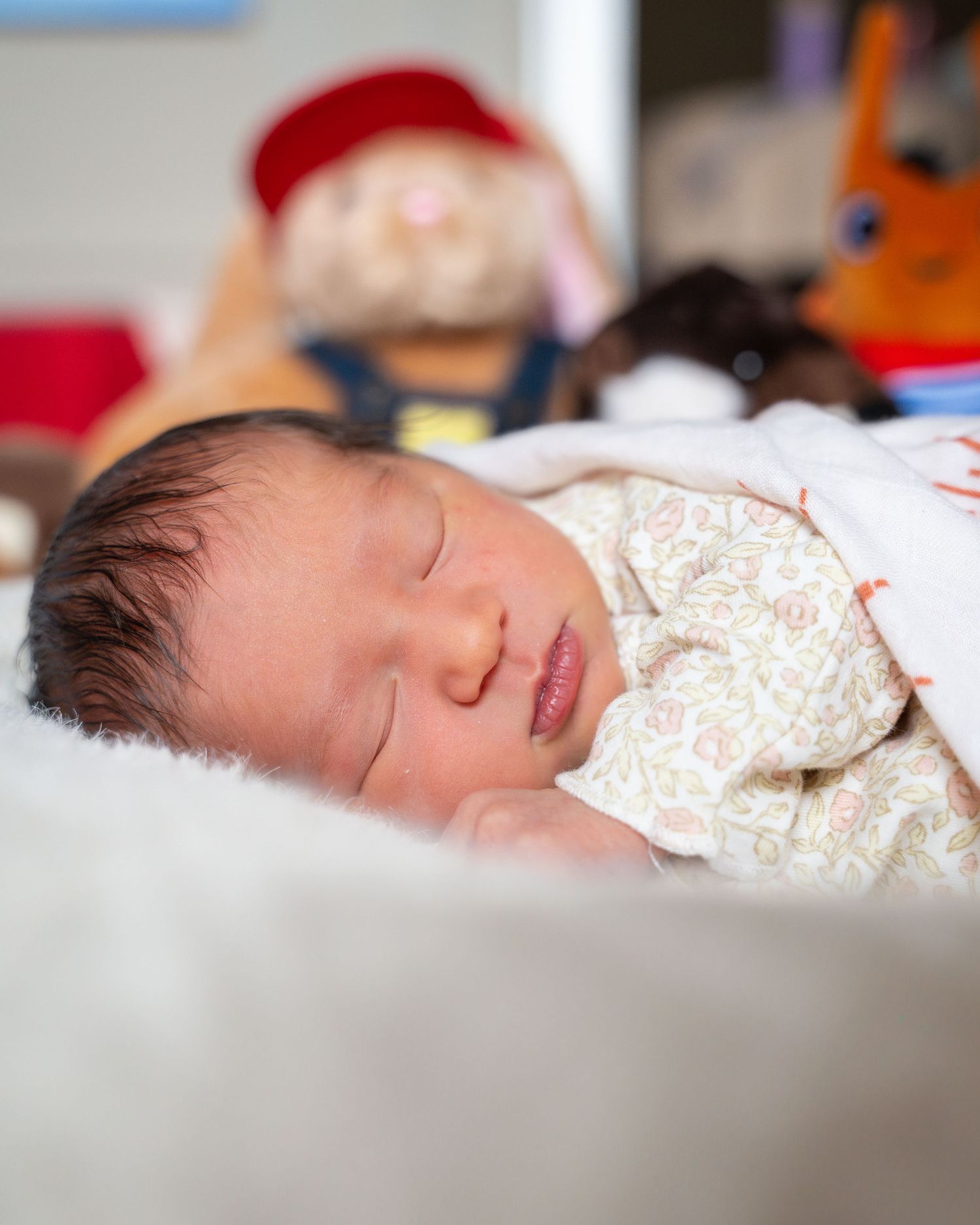 A sleeping infant rests peacefully on white bedding while wearing a patterned onesie.