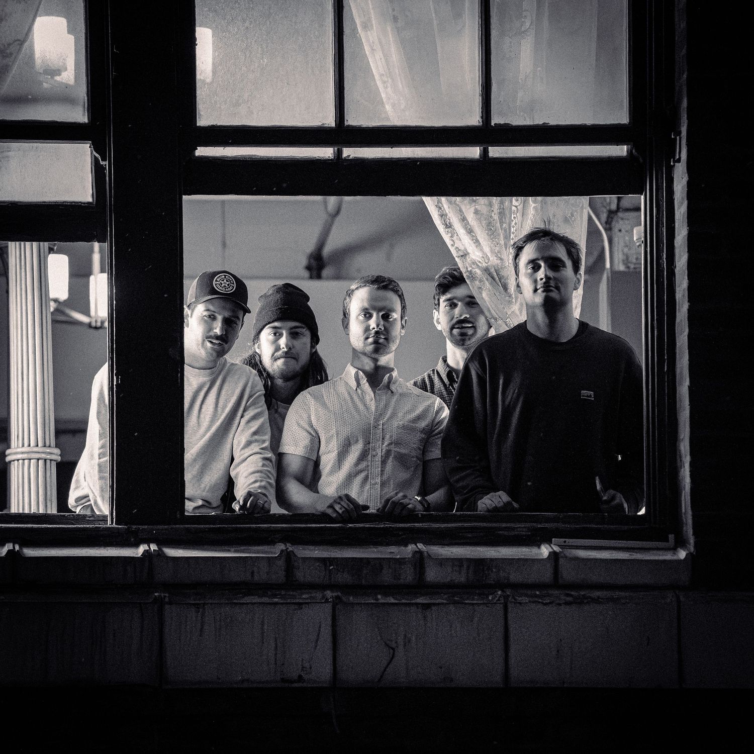 Black and white photo of a music band posing together in a window frame.