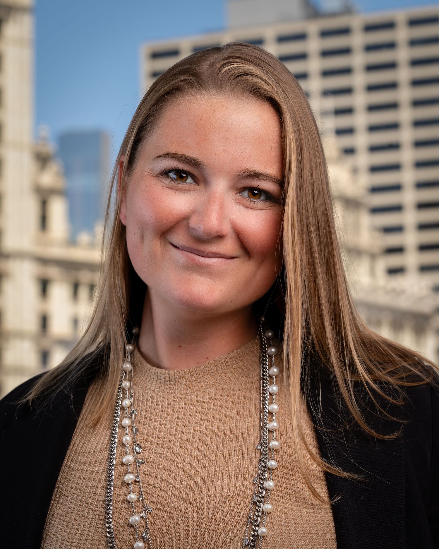 Professional portraits with beige sweater and statement necklace against urban setting.