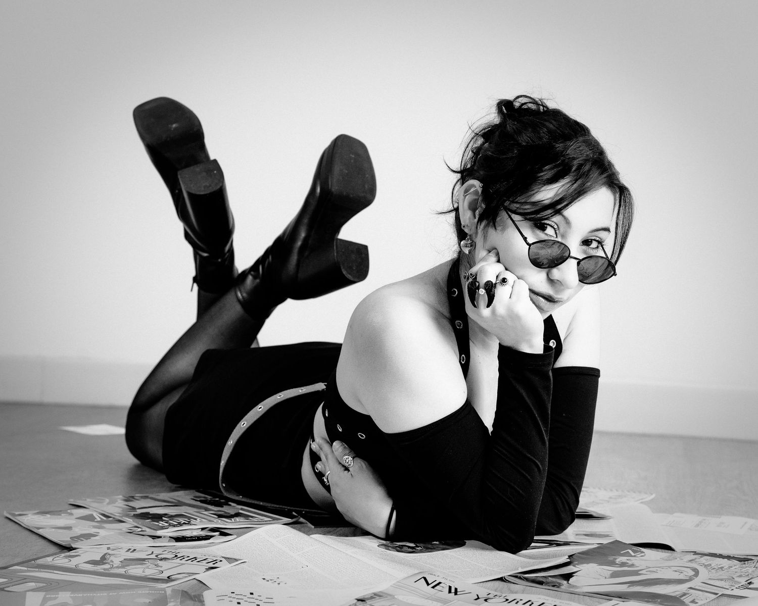 Black and white fashion photo lying on newspaper in boots and sunglasses.