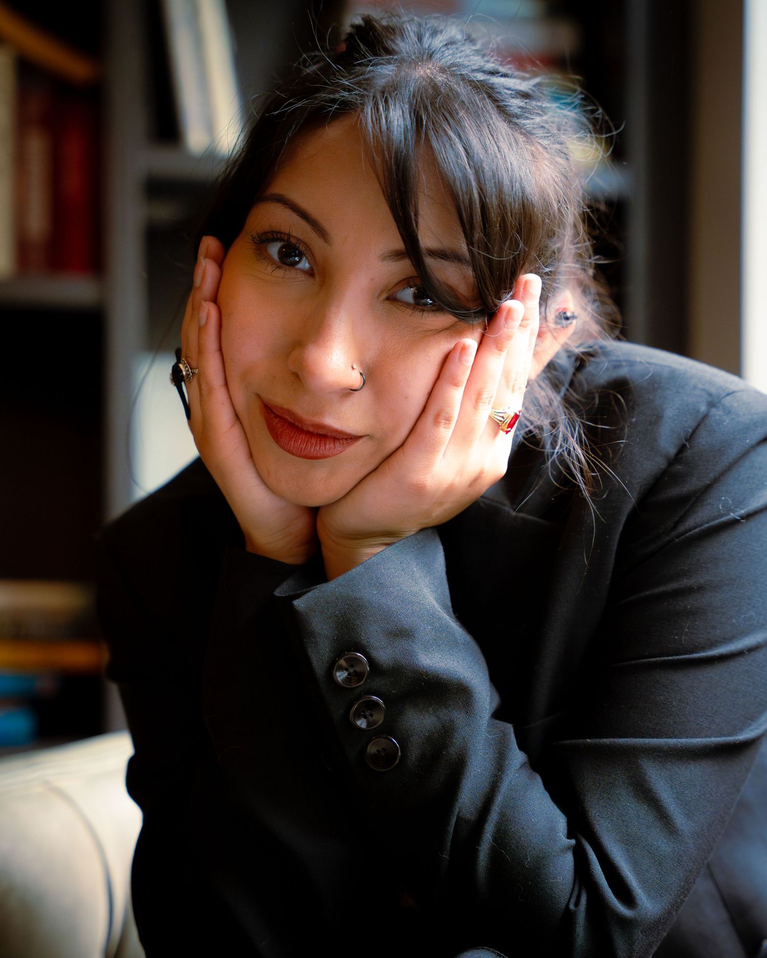 Cozy indoor portrait showing relaxed pose against bookshelf background.