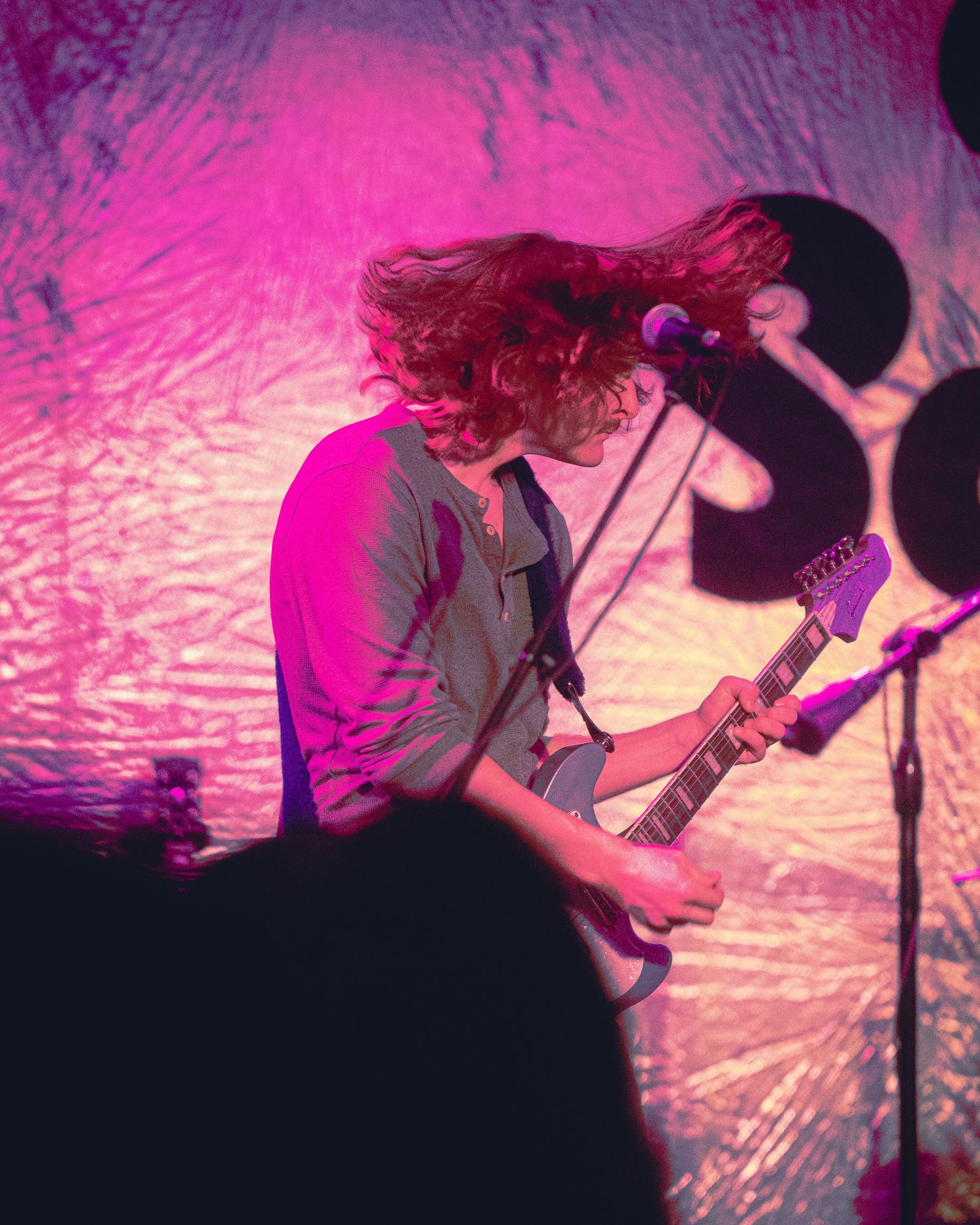 Silhouetted musicians performing on stage with vibrant pink and purple lighting creating a dramatic atmosphere.