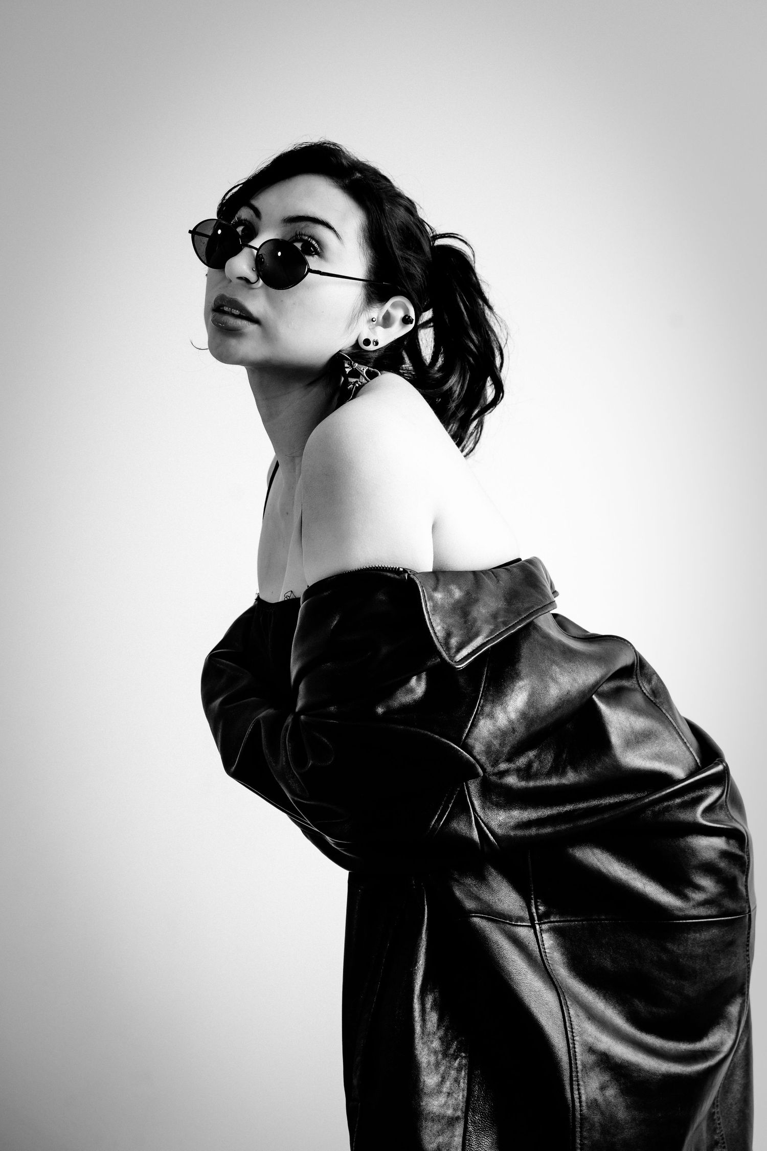 Dramatic black and white fashion portrait with leather jacket and sunglasses against light background.