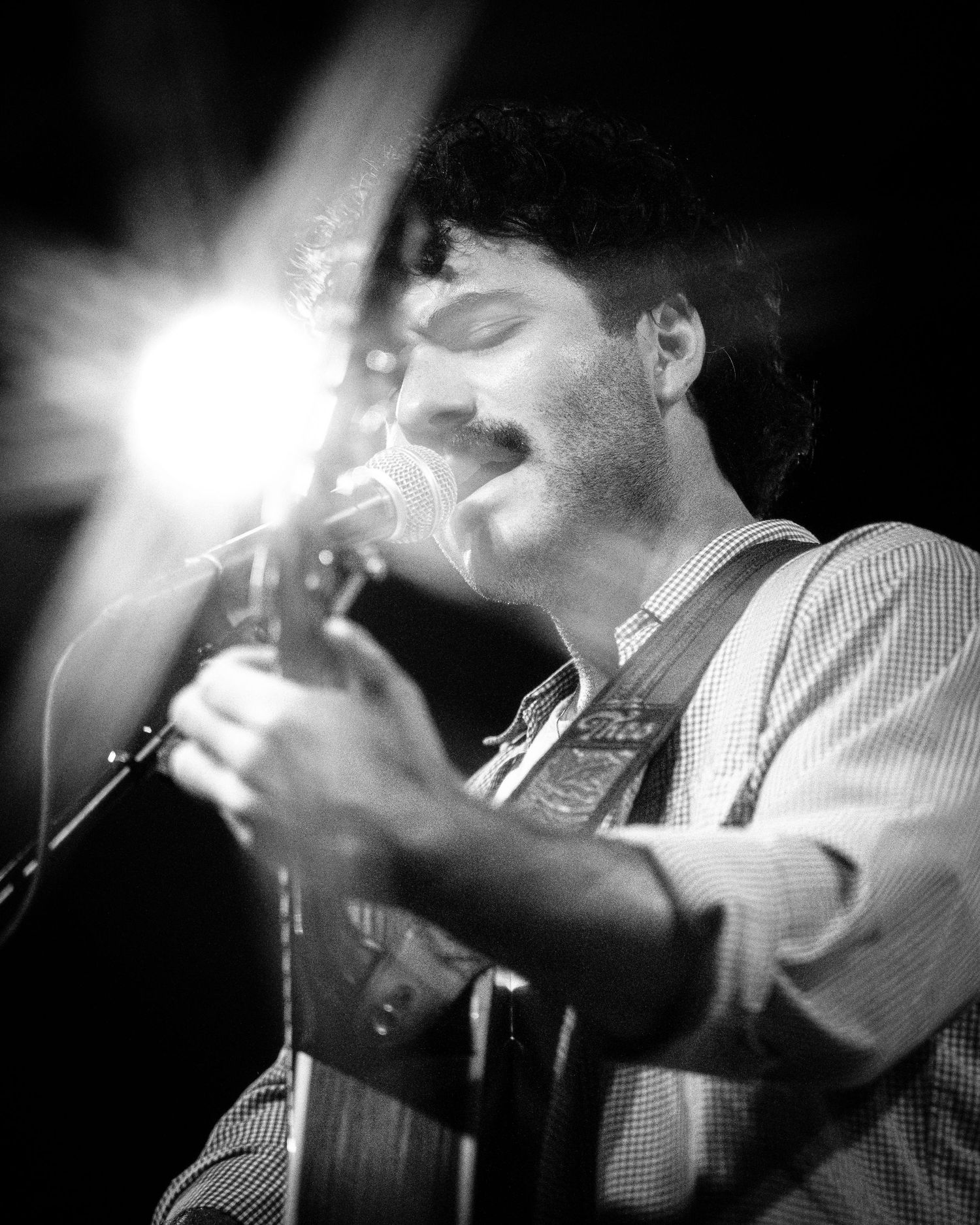 Black and white photo of musician performing passionately on acoustic guitar with dramatic lighting.