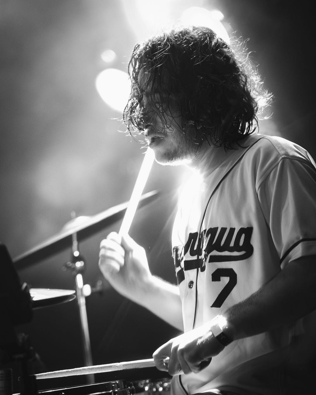 Black and white shot of a performer playing drums during a concert with dramatic stage lighting.