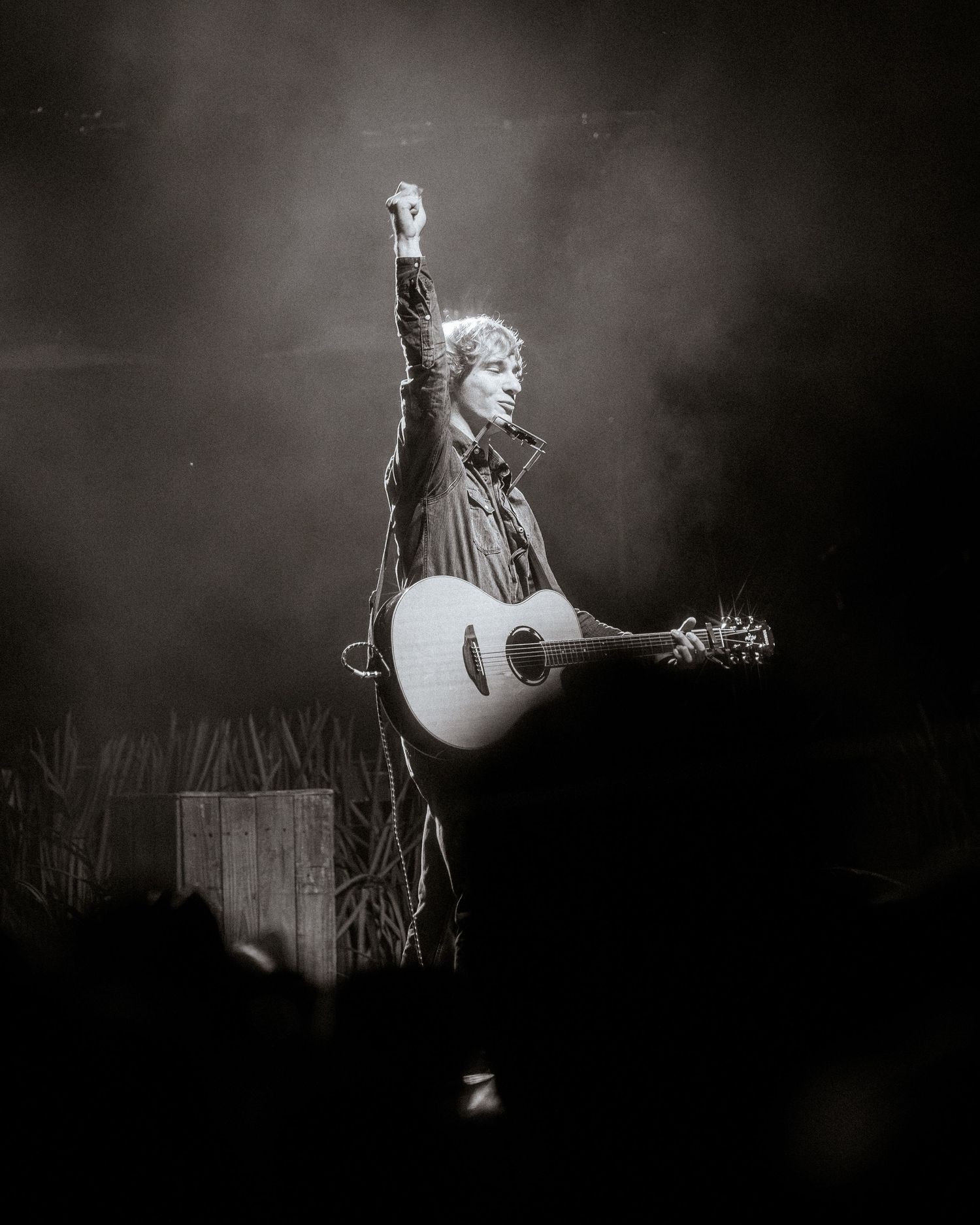 Black and white concert photo showing performer with acoustic guitar in dramatic stage lighting.