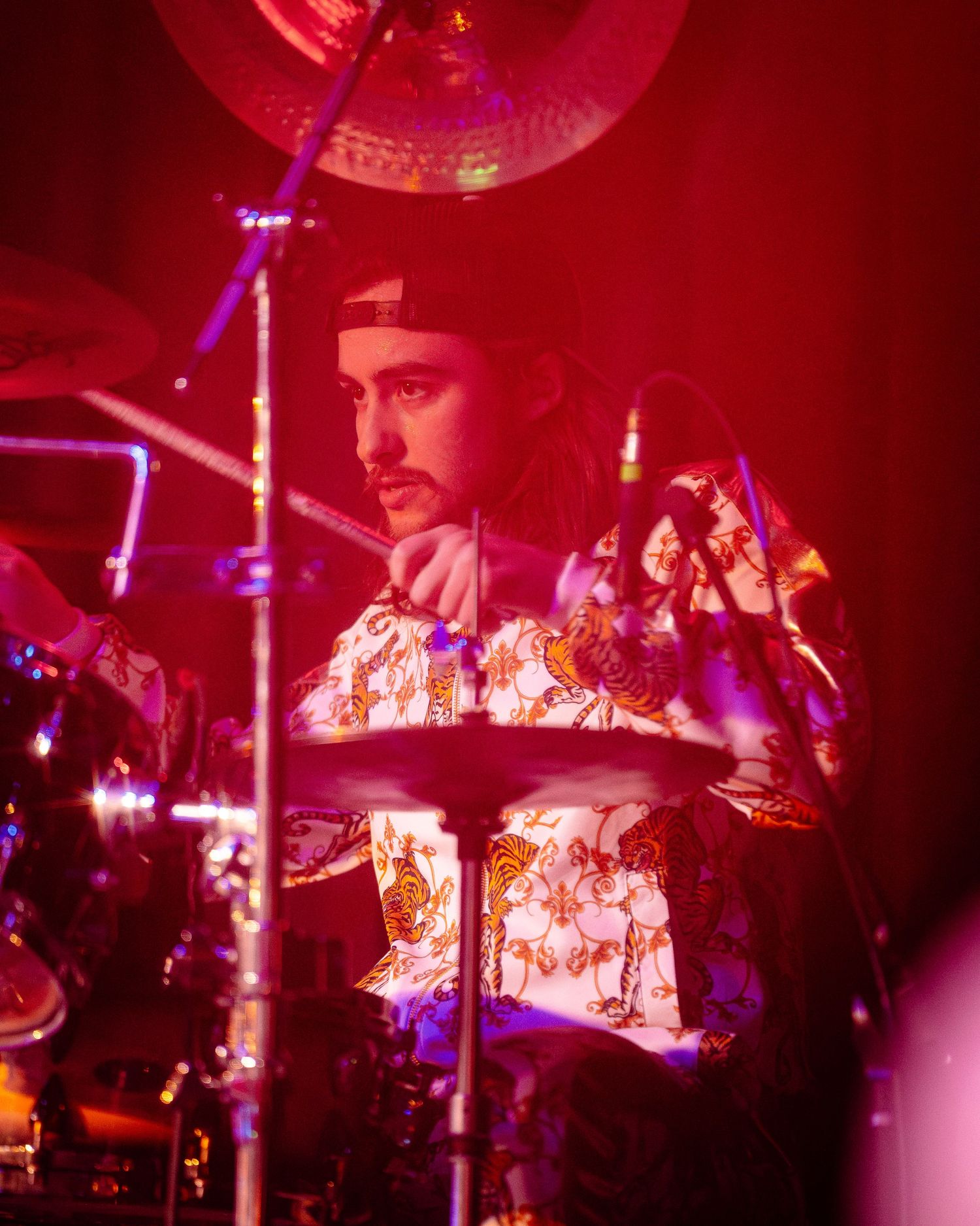 Drummer performing on stage bathed in deep red lighting effects.