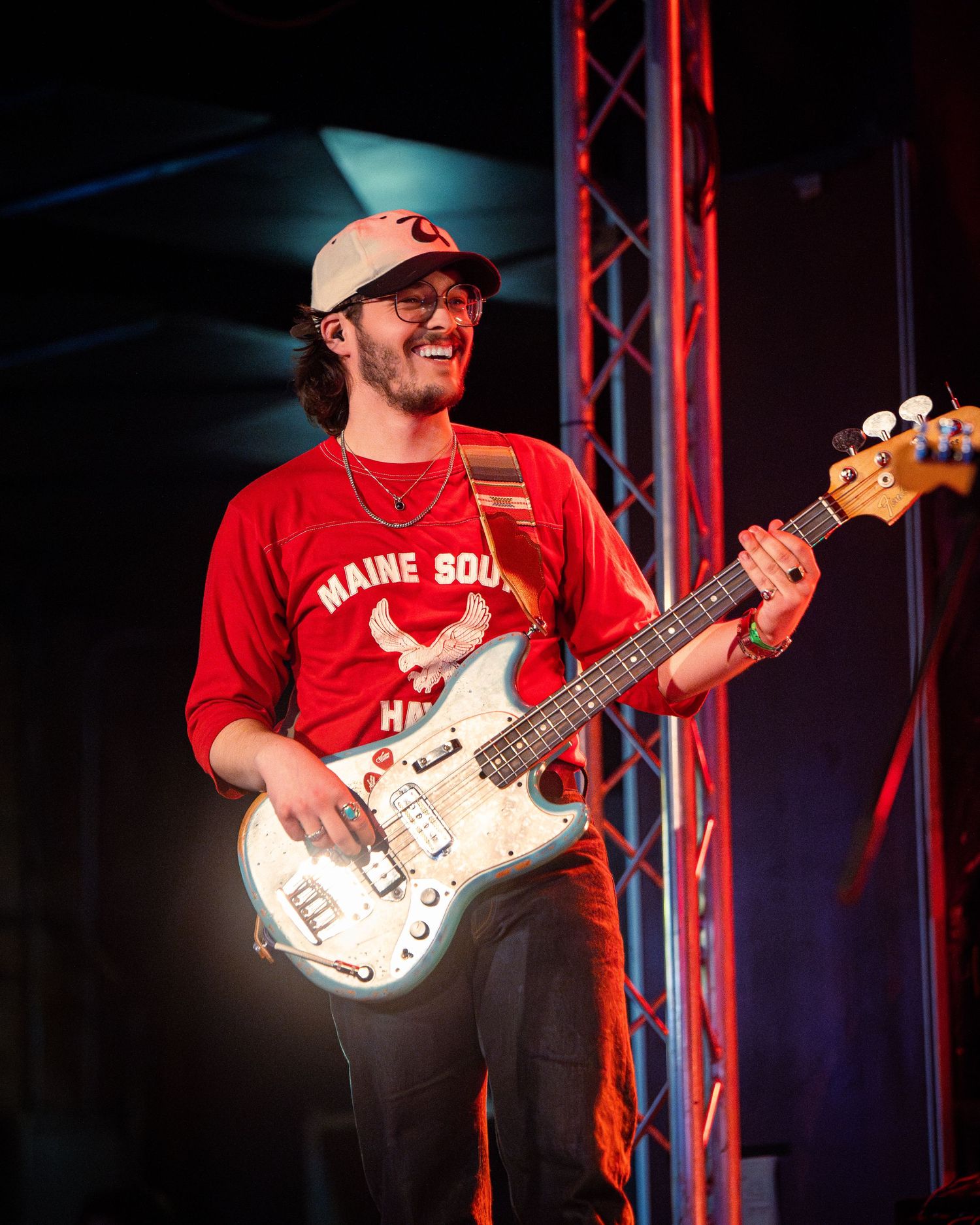 Bass player holds white instrument while performing under stage lights.