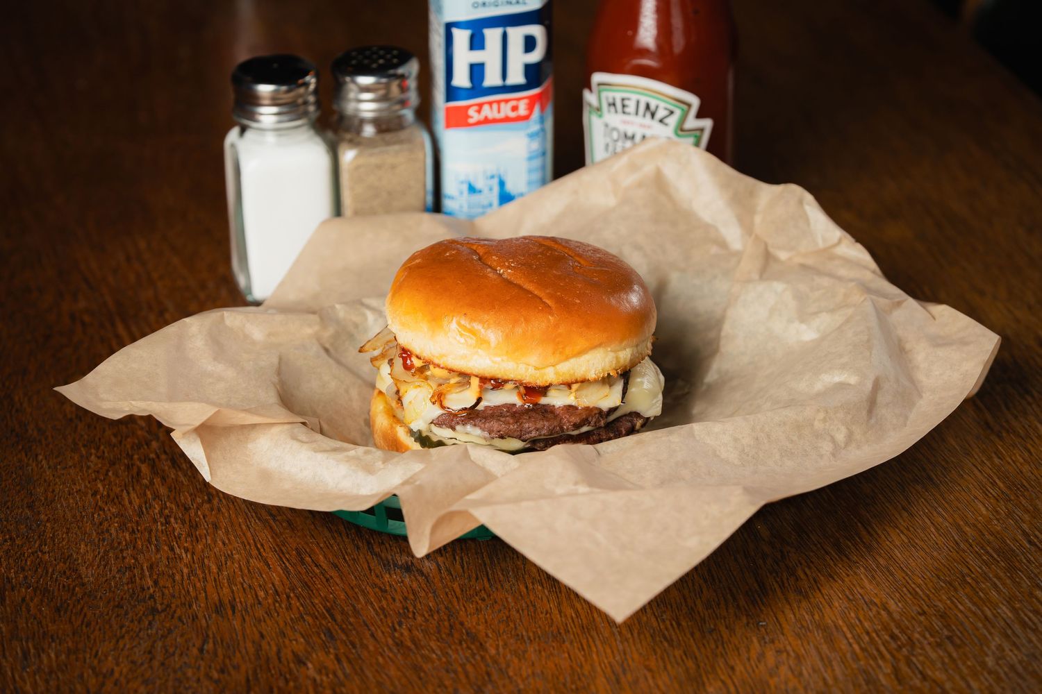 Juicy cheeseburgers and sides served on brown paper with condiments and drinks in the background.