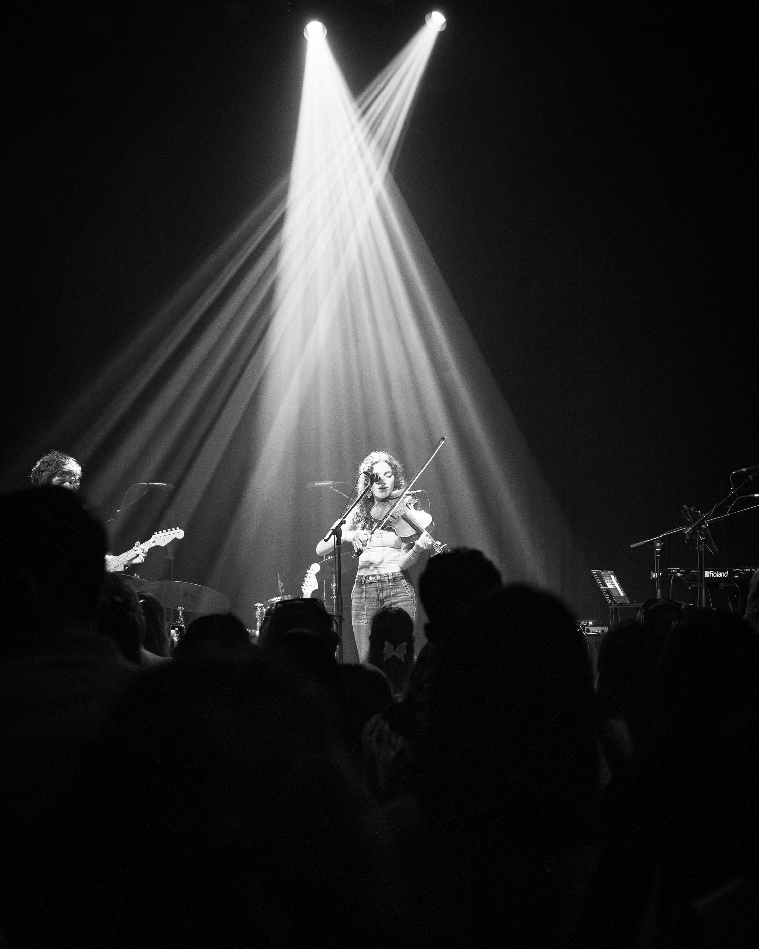 Concert stage illuminated by intersecting white spotlights creating dramatic beams over the audience.