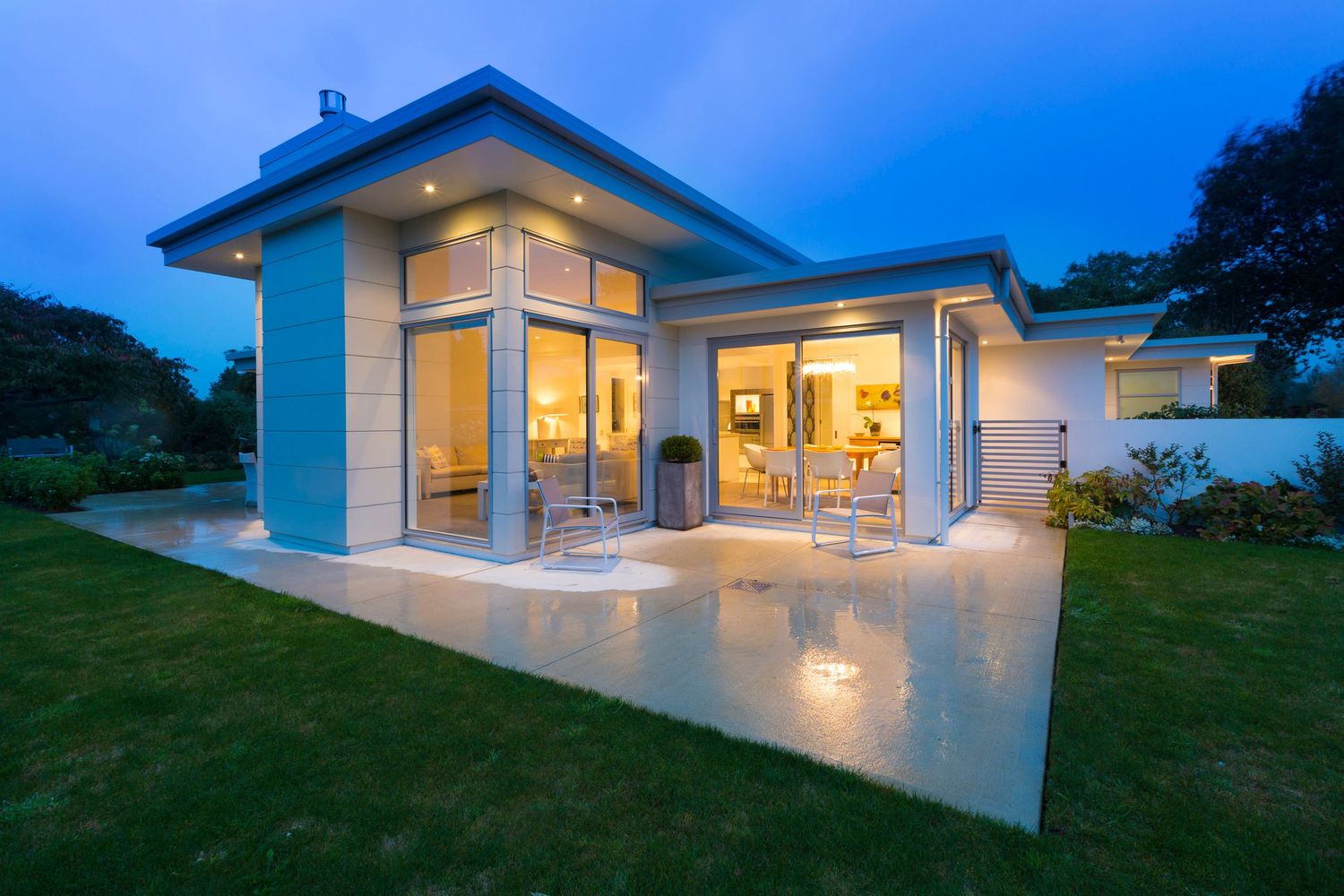 Contemporary glass house with pool deck illuminated at dusk.