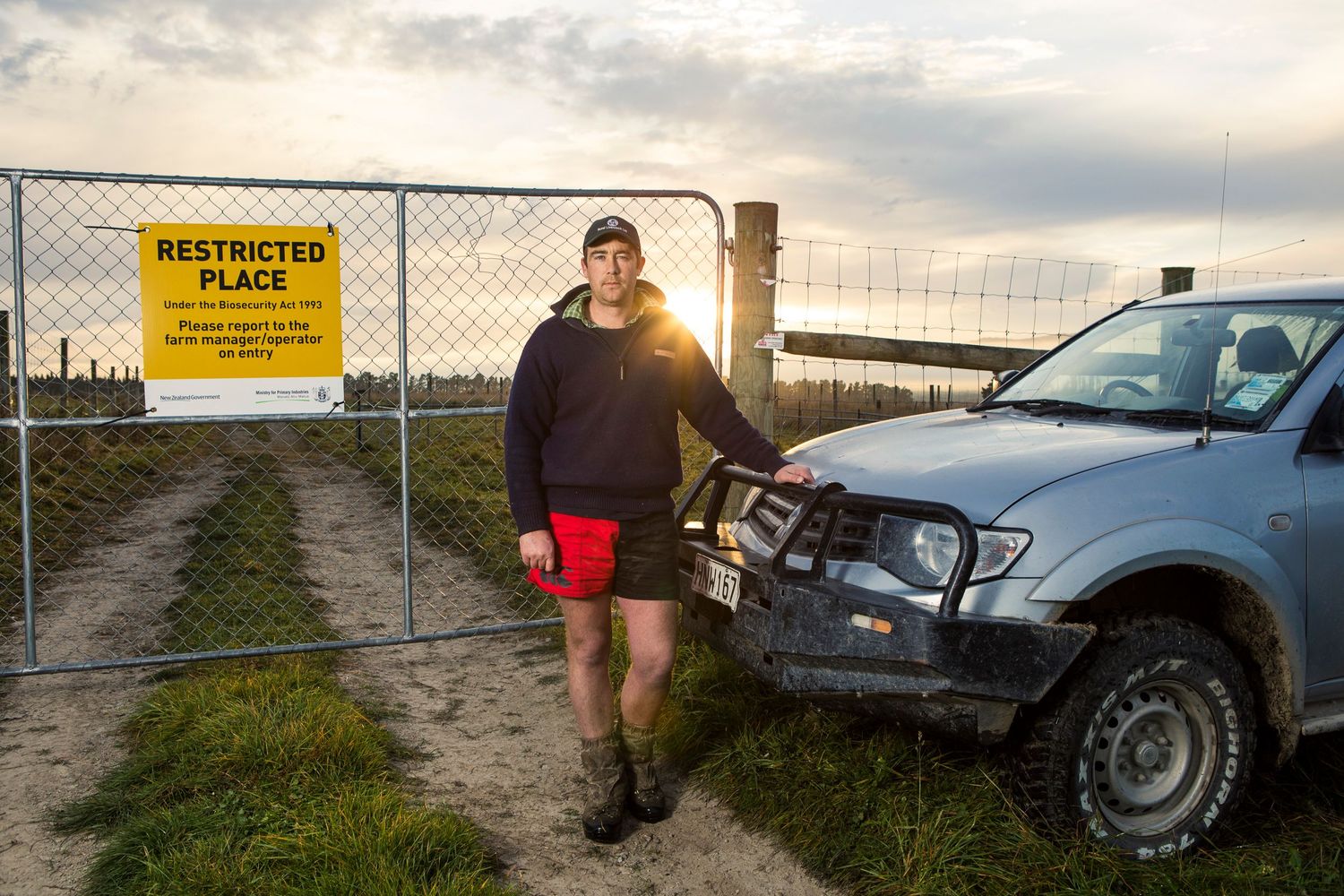 4x4 vehicle parked by farm gate with warning sign during sunset.