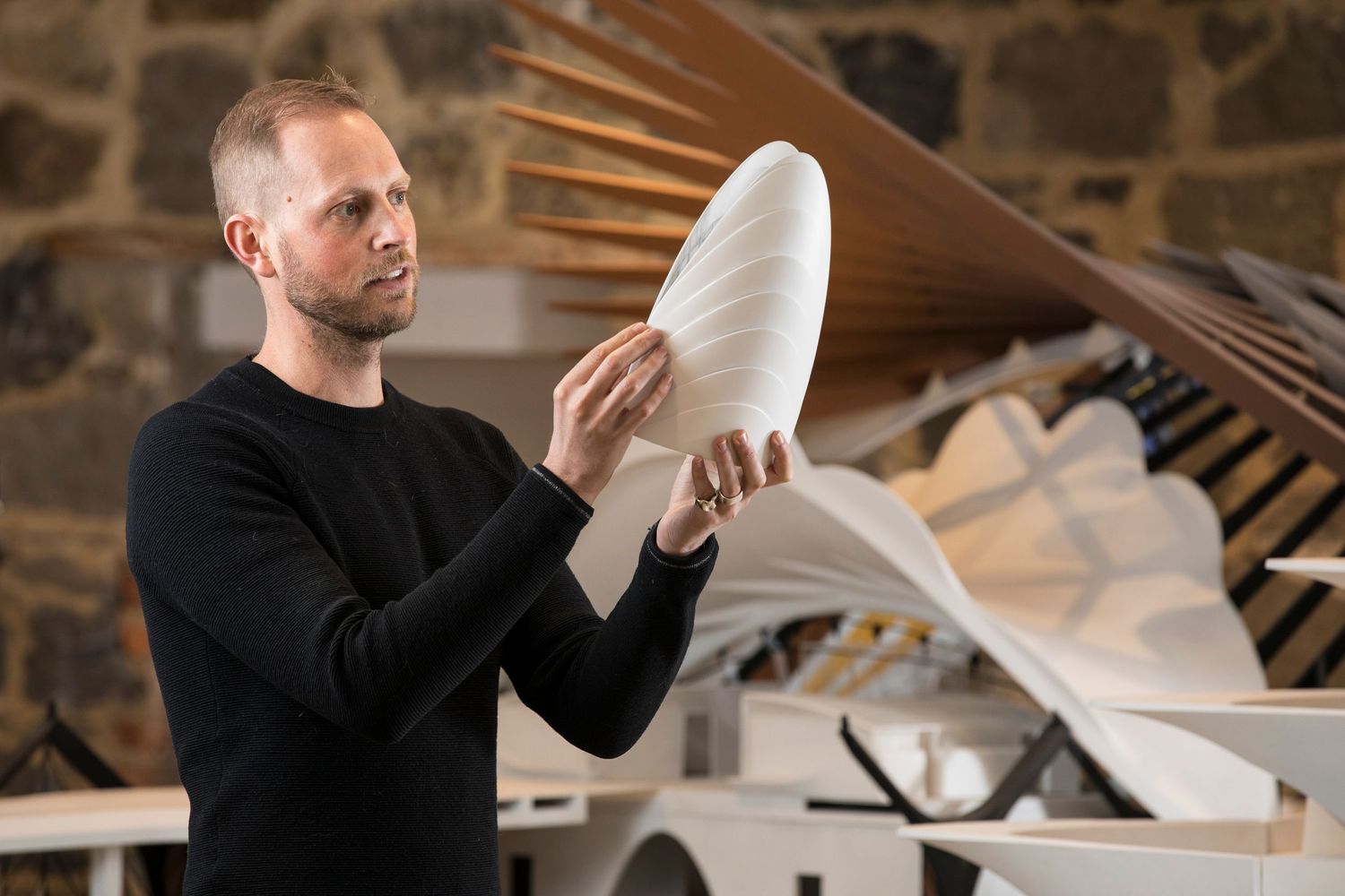 Craftsman examining a large white sculptural piece in stone-walled workshop.