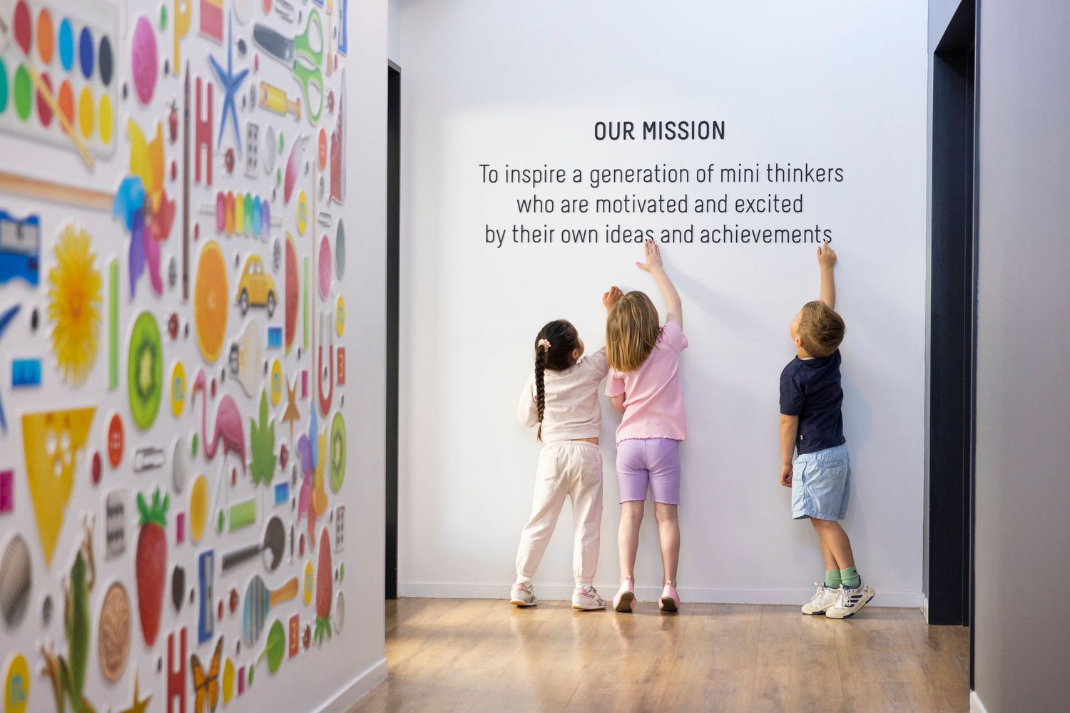 Children pointing at colorful wall art display in children's educational space.