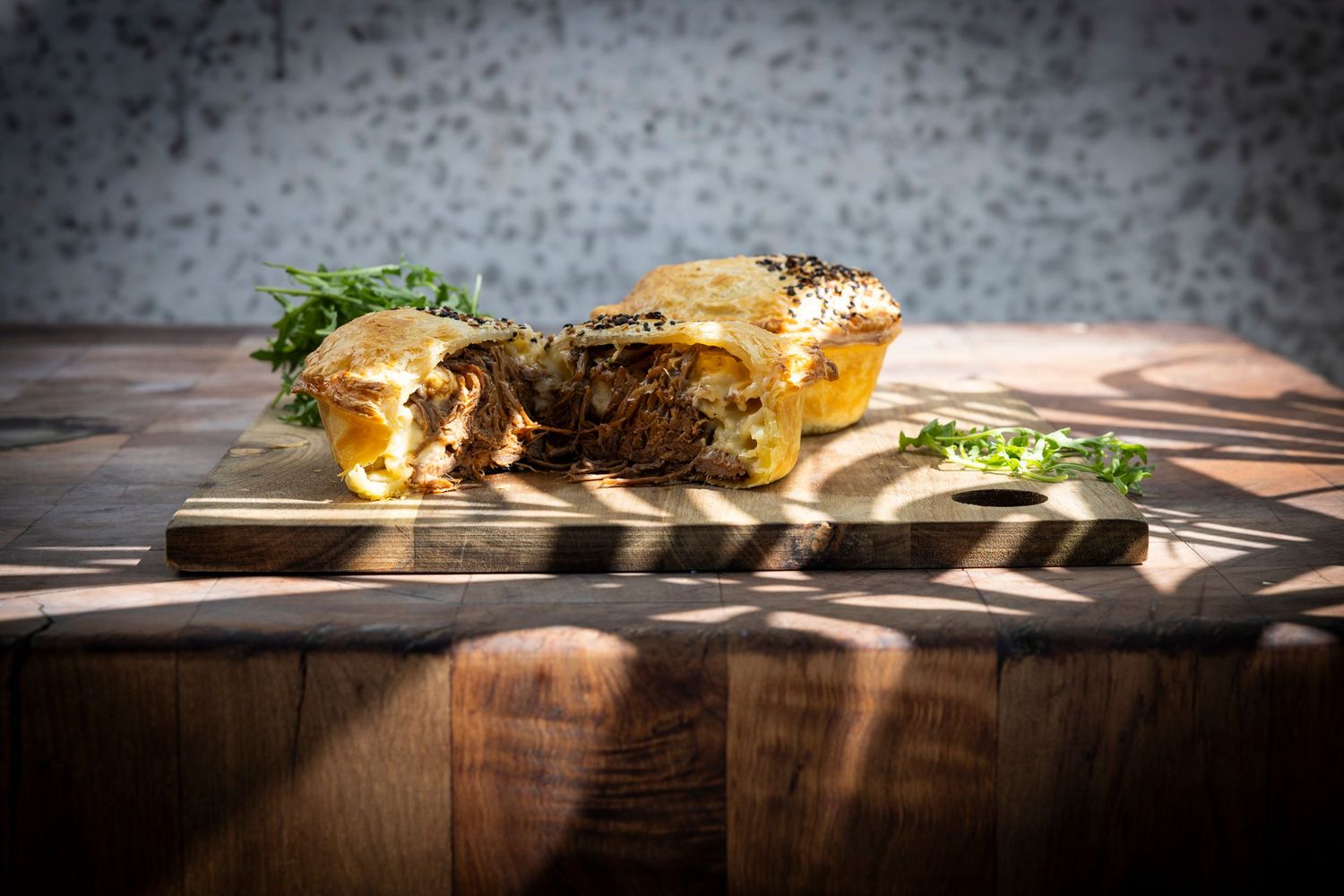 Gourmet pie cut in half showing meat filling on a wooden cutting board with dramatic lighting.