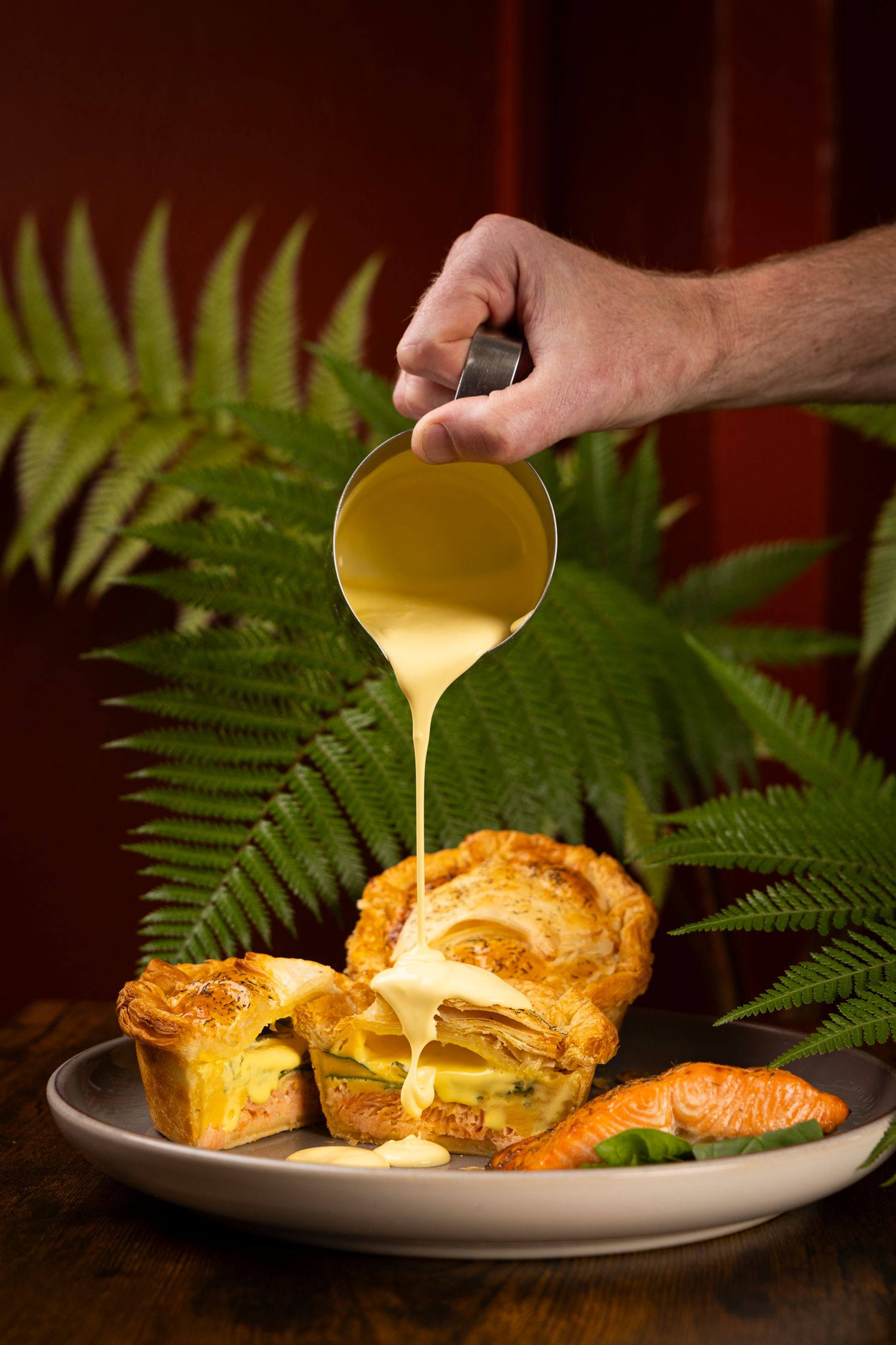 Golden sauce being poured over a freshly baked pastry with ferns in the background.