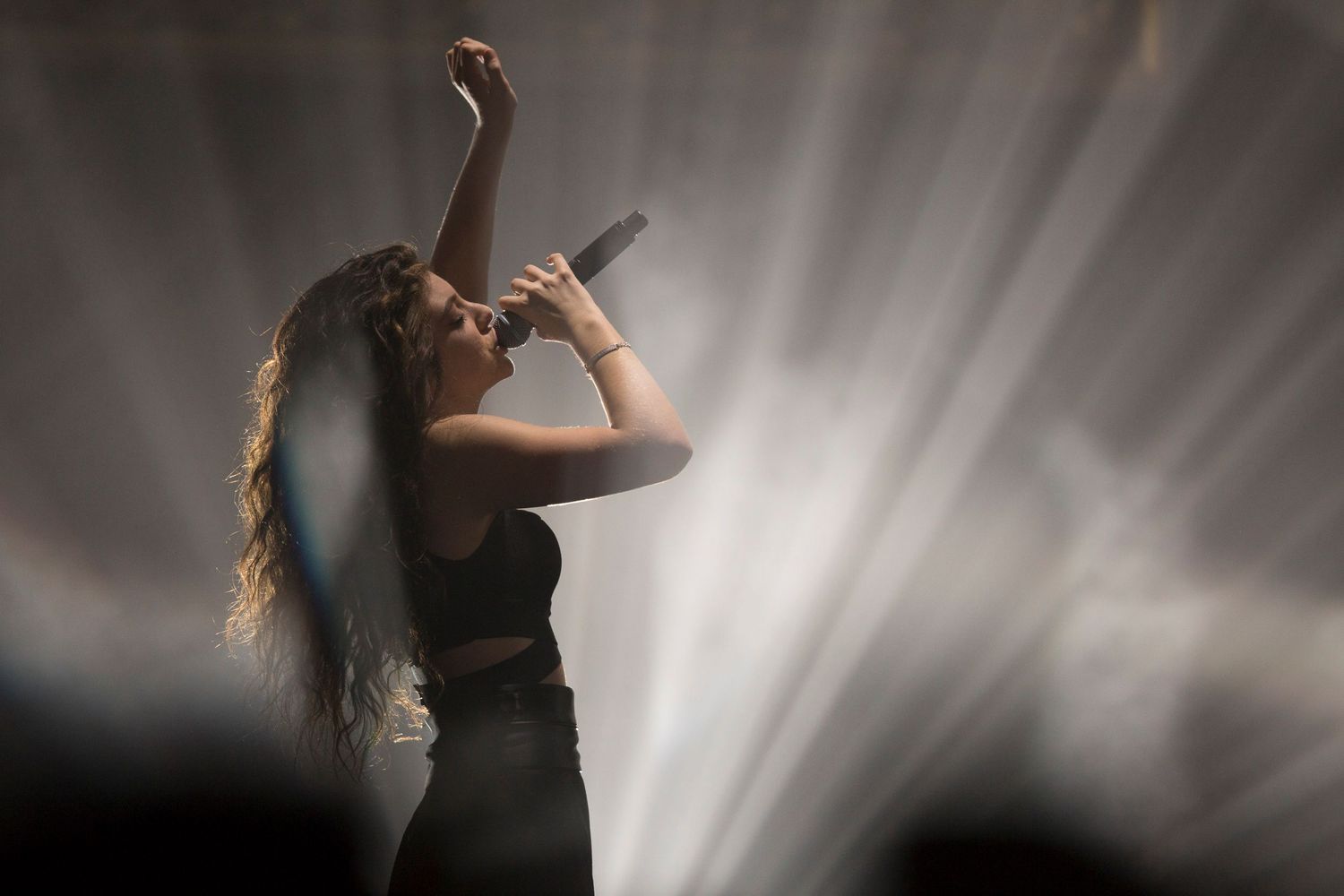 Silhouetted performer with long hair singing on stage with dramatic backlighting.