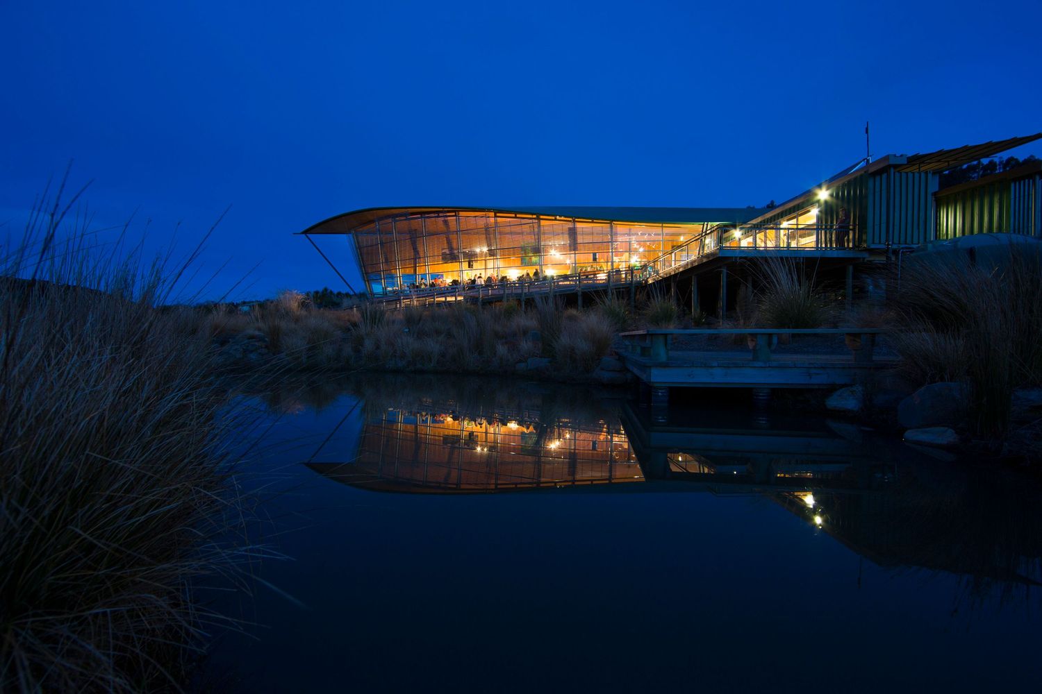 Illuminated modern building exterior with curved architecture glowing against dark blue twilight sky.