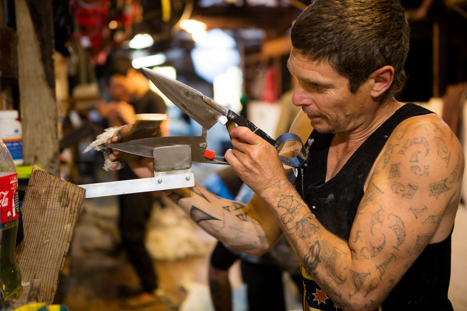 Craftsman with tattooed arms examining metal tools in workshop setting.