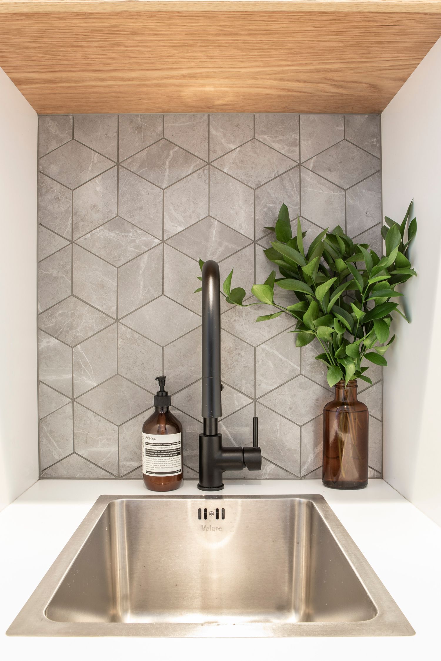 Modern kitchen nook featuring geometric tile backsplash, matte black faucet, stainless sink and wooden ceiling accent.
