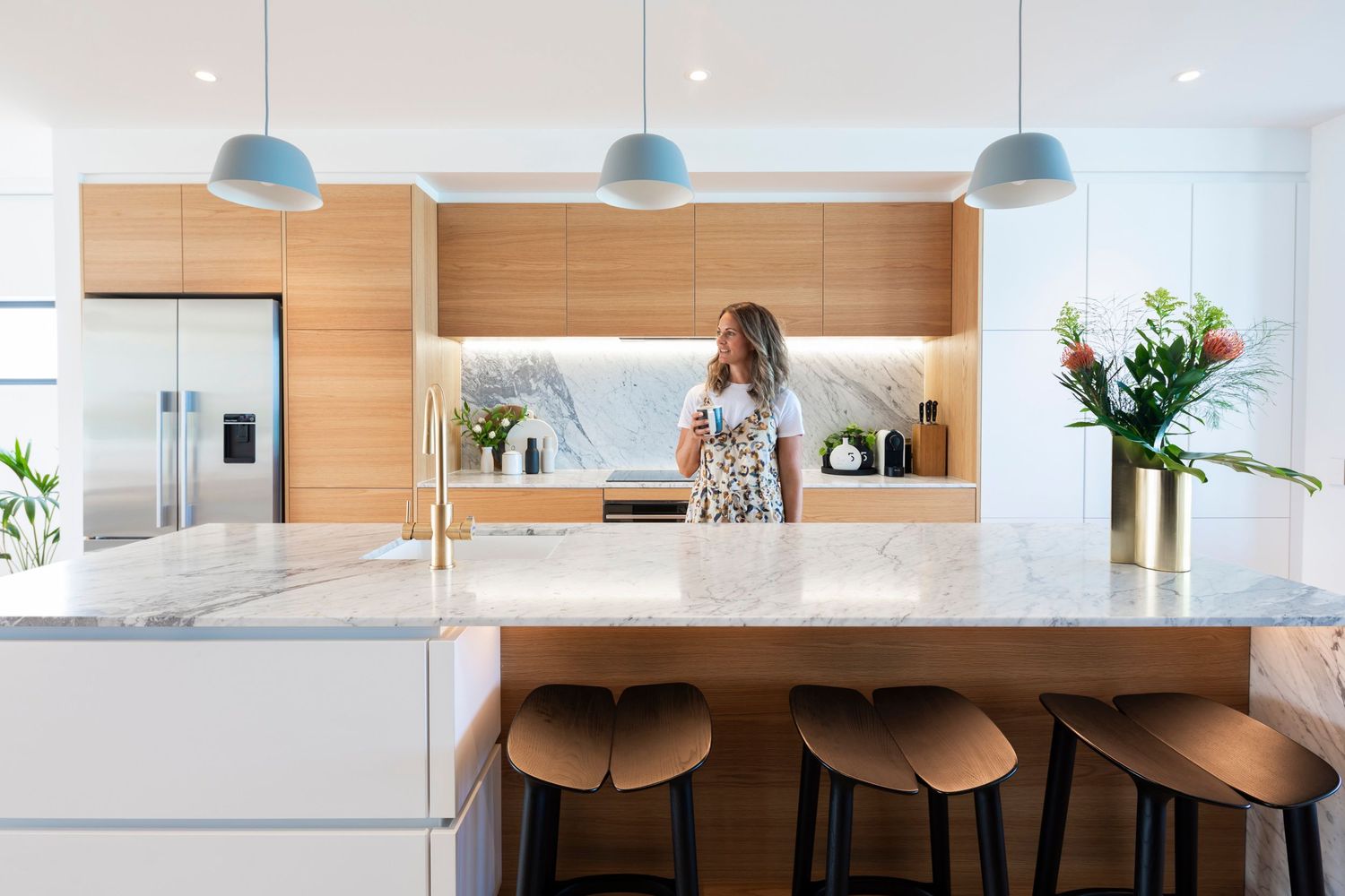 Modern kitchen featuring white marble countertops and wood accents with pendant lighting.
