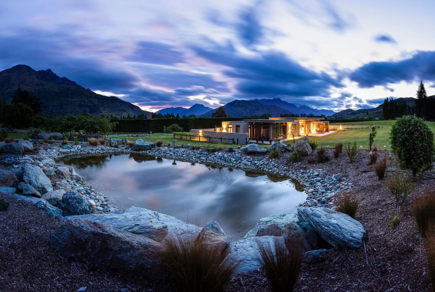 Panoramic view of a luxury lakeside residence with mountain views at twilight.