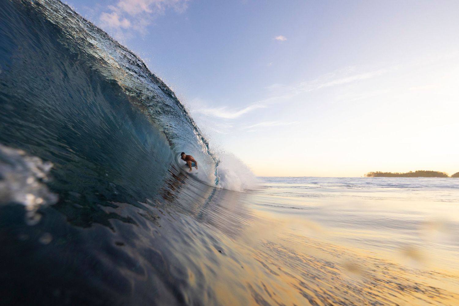 Curling ocean wave at sunset with golden light shining through the water.
