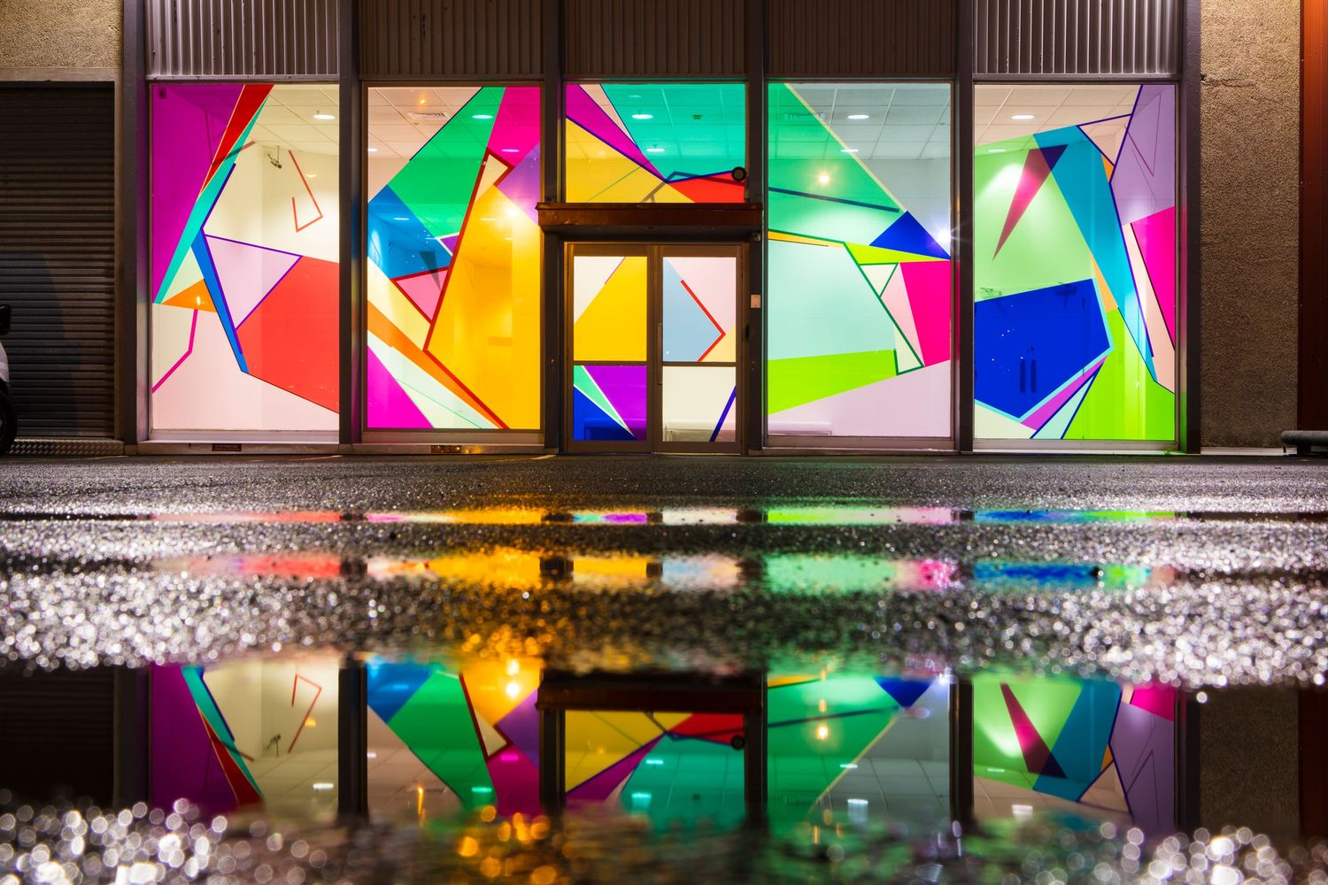 Colorful abstract geometric art installation illuminated along interior wall display.