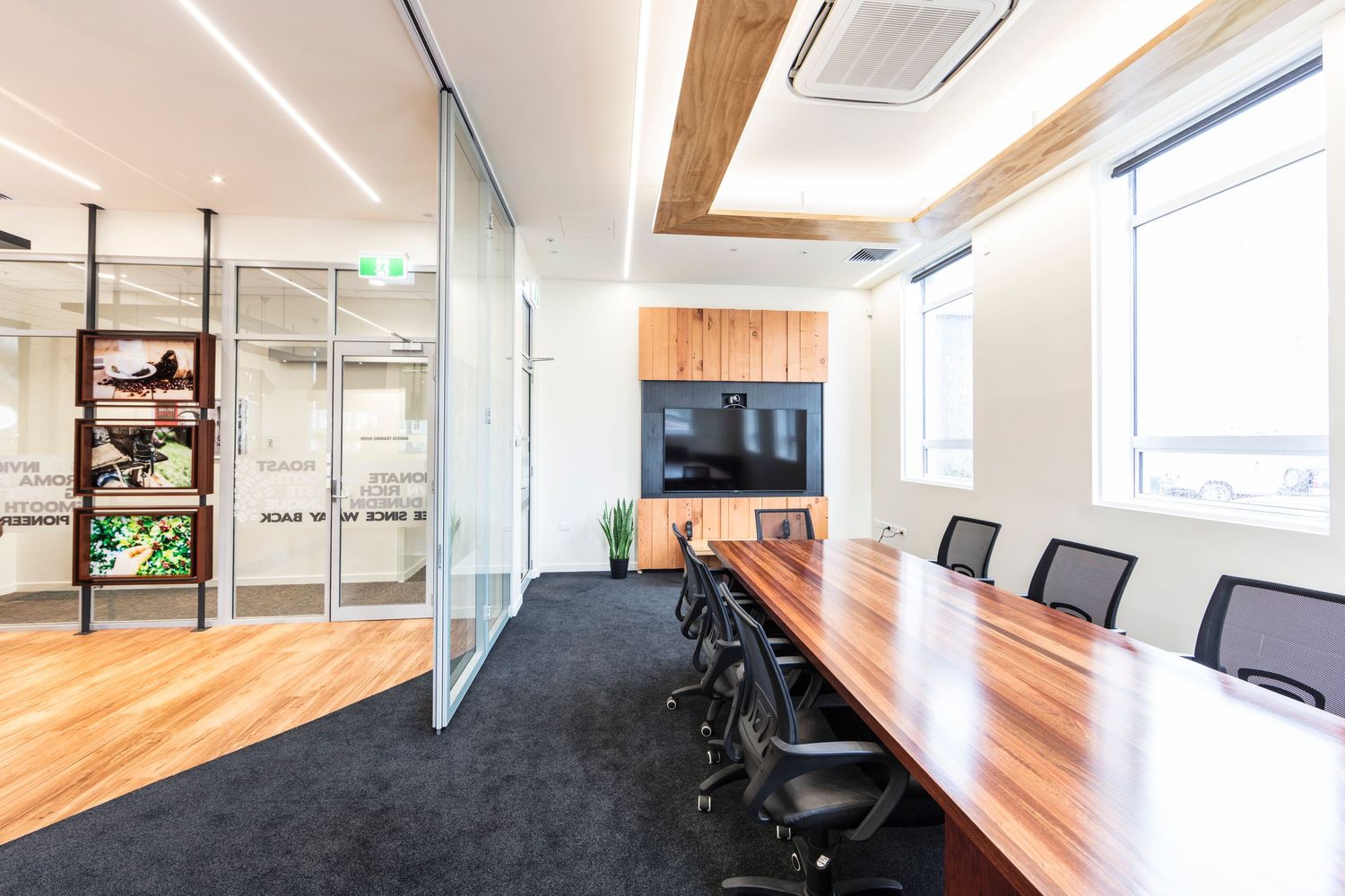 Contemporary meeting room with wooden conference table and black chairs next to glass partition wall.