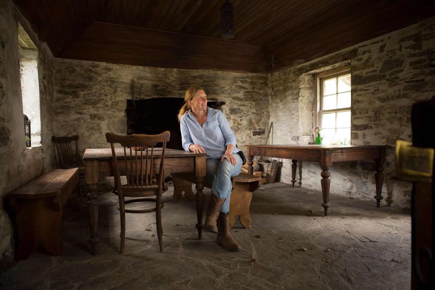 Interior of rustic stone cottage with wooden furniture and natural window light.