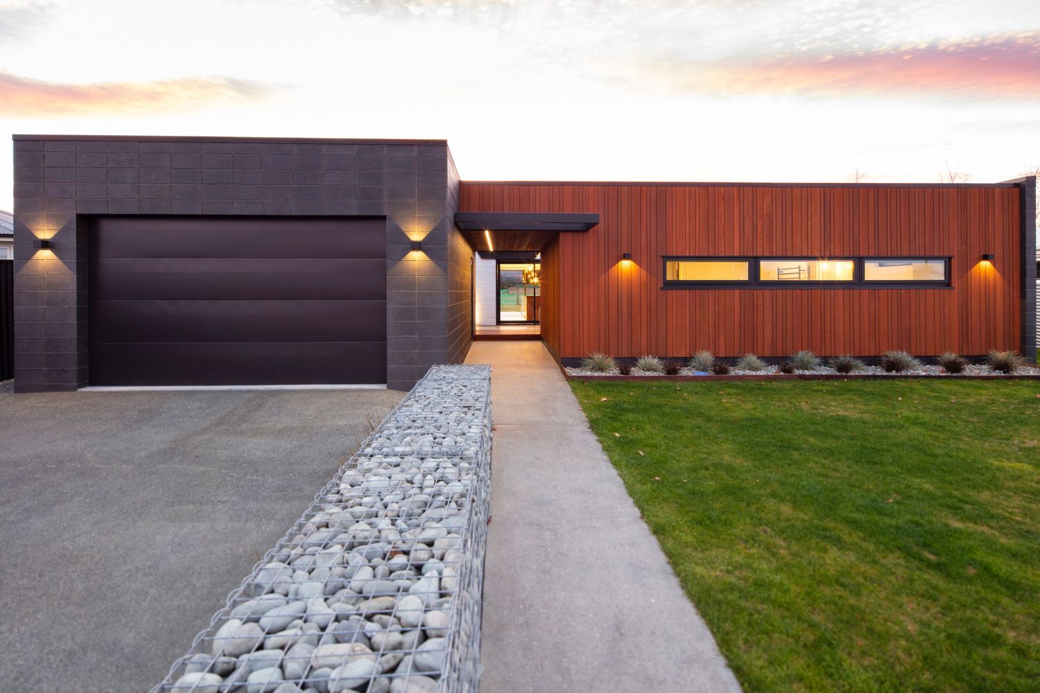 Modern home exterior featuring stone pathway and dramatic architectural lighting.