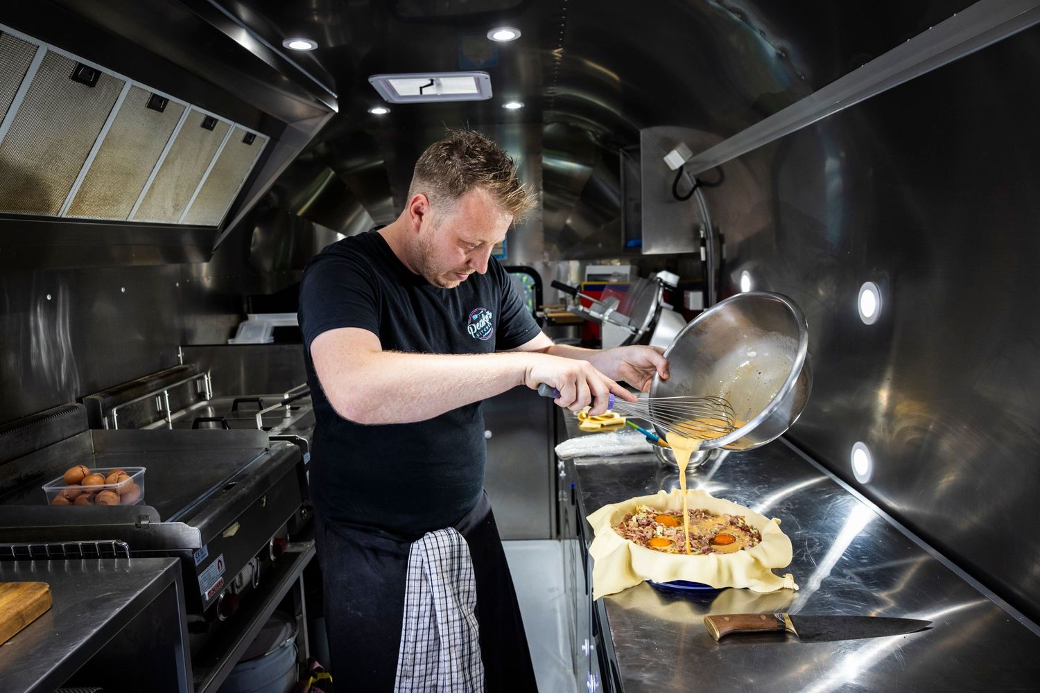 Chef cooking in commercial food truck kitchen with stainless steel equipment.