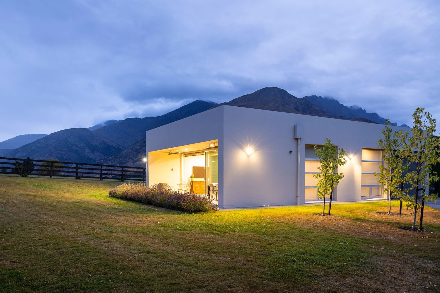 Contemporary white house illuminated at dusk with mountain ranges in the background.
