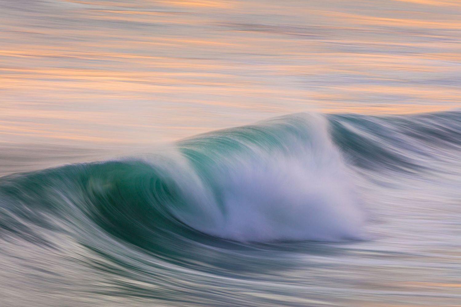 Rolling ocean wave catches golden sunset light creating peaceful seascape with pastel colors.