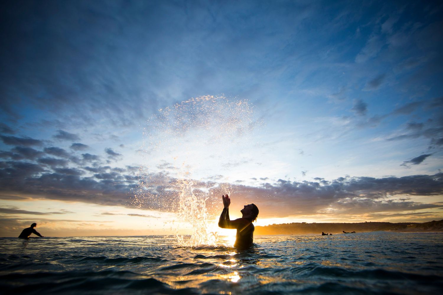 Silhouette splashing water in ocean at sunset with dramatic cloudy sky.