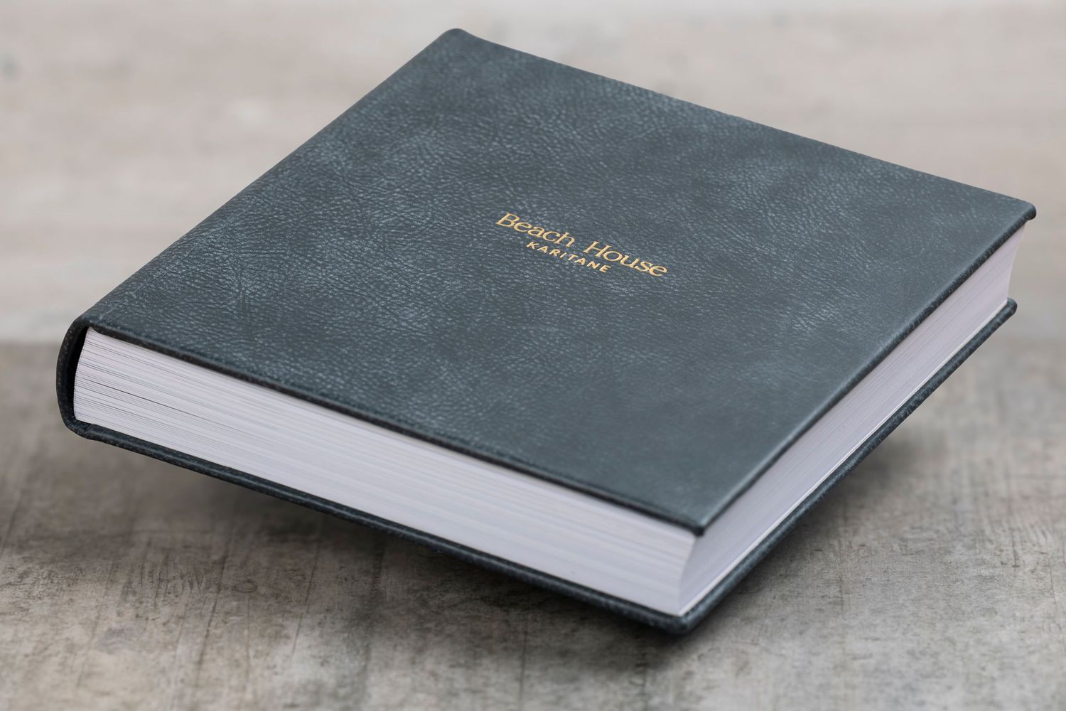 A modern photo album with gray linen cover shown from multiple angles on a concrete surface.