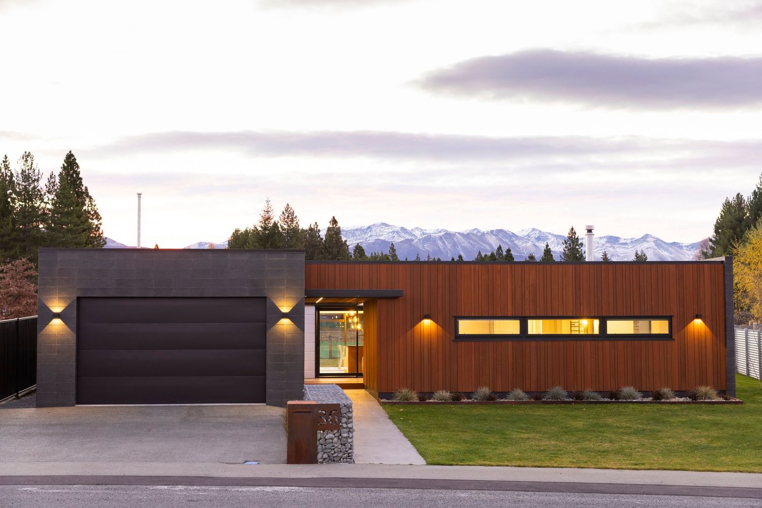Sleek modern house exterior with dark and wood-toned cladding against mountain backdrop.