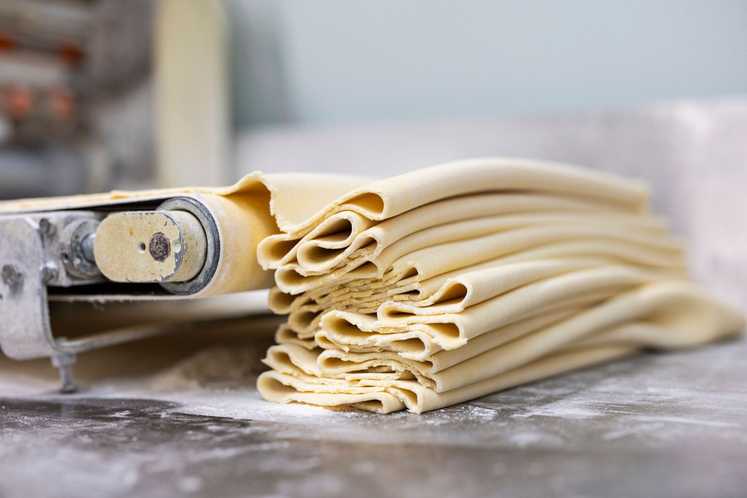 Fresh pasta dough being rolled out on a floured surface in sequential steps.