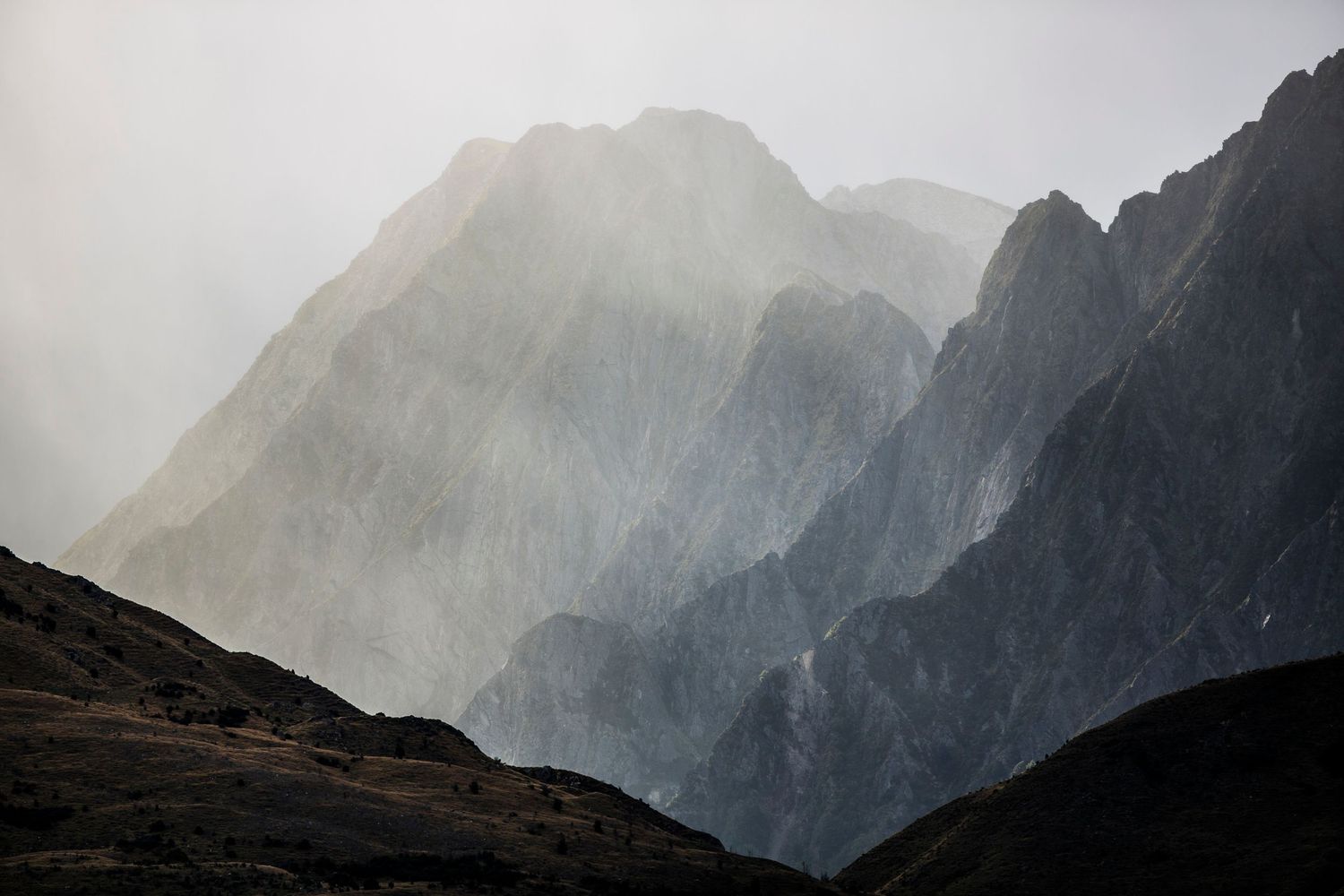Misty mountain peaks rise dramatically through fog in moody atmospheric conditions.