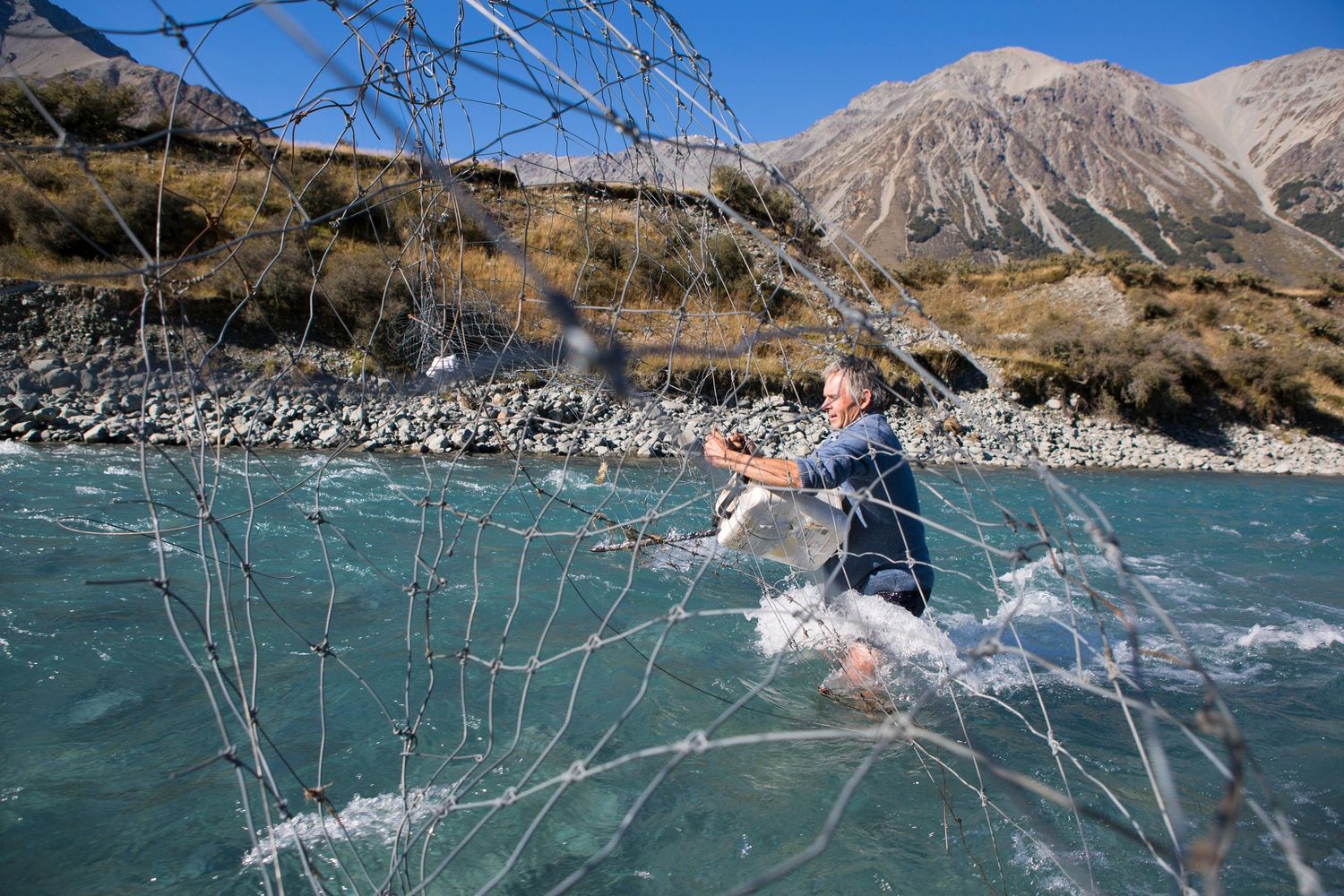 Person splashing through turquoise glacial river with mountains in background.