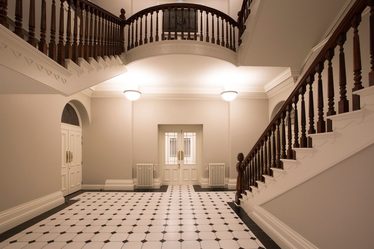 Elegant foyer with black and white checkered floor and curved wooden staircase with white walls.