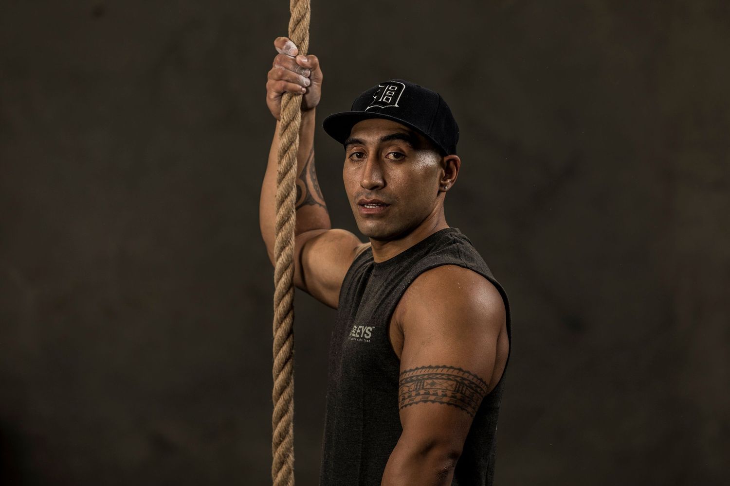 An athlete grips a climbing rope against a dark background showing strength and determination.