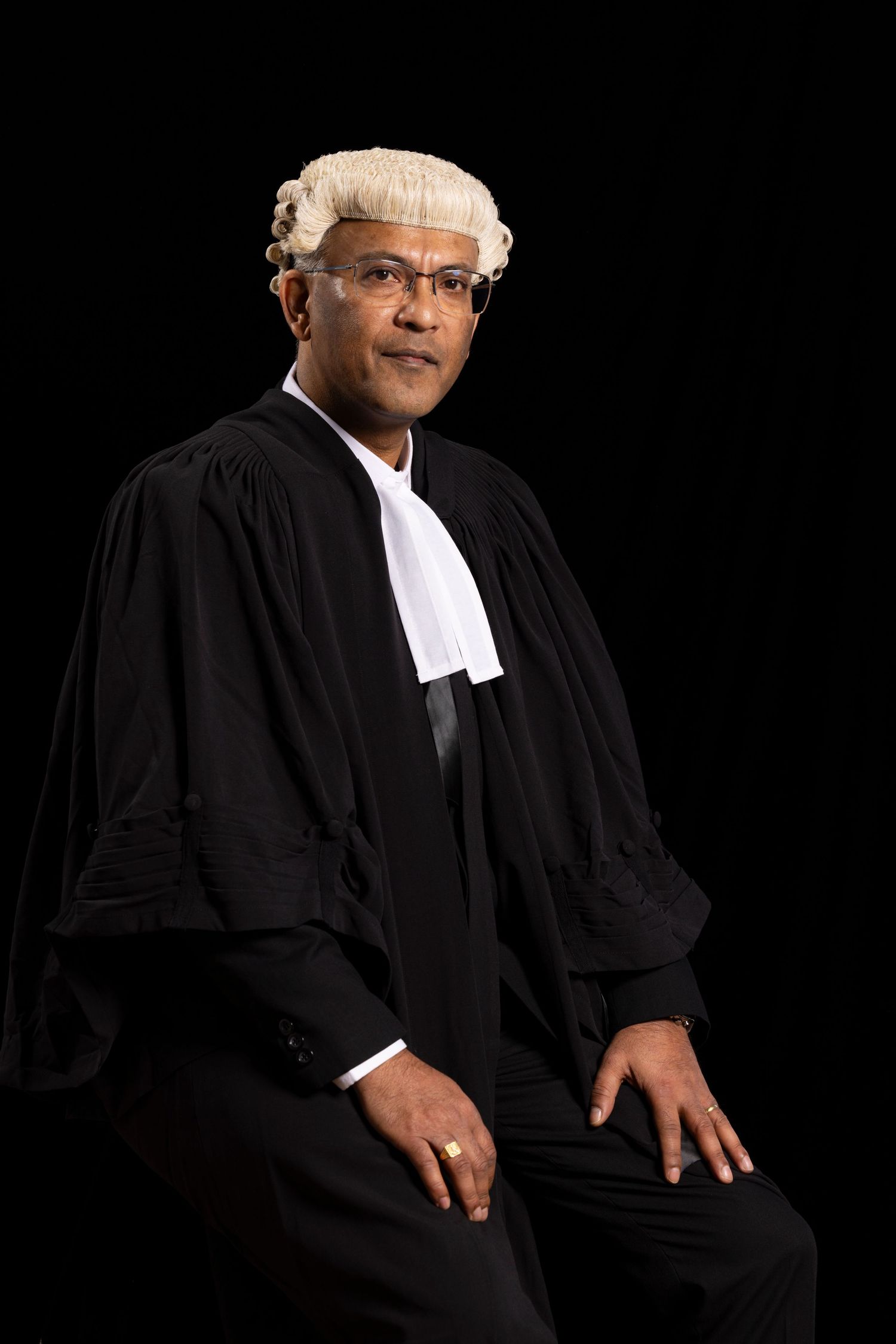 Judge in traditional court attire seated against black background.