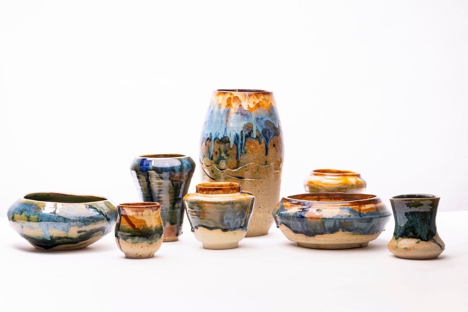 Collection of handcrafted ceramic vessels with blue and orange drip glaze patterns.