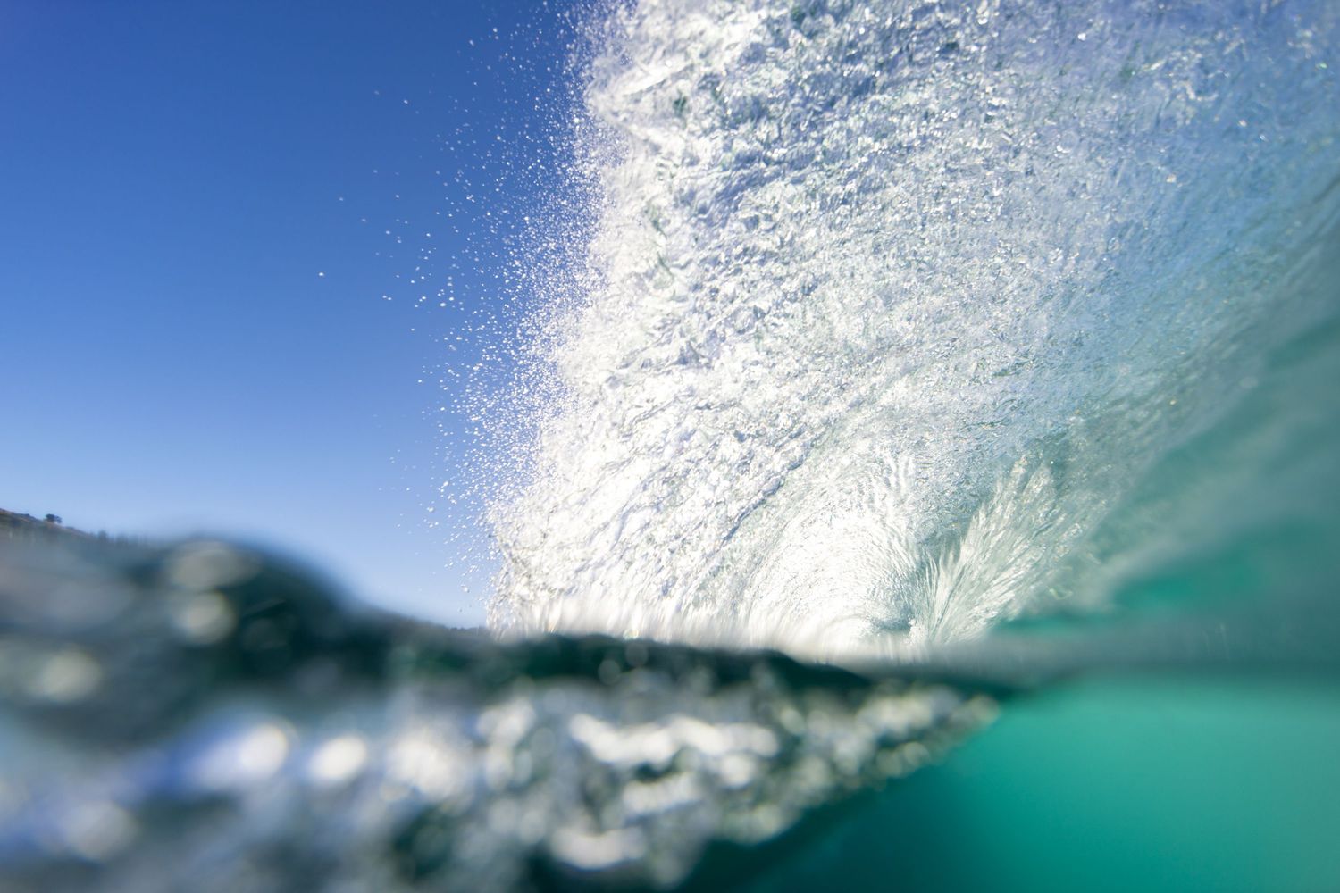Crystal clear turquoise wave crashes with white foam against bright blue sky.