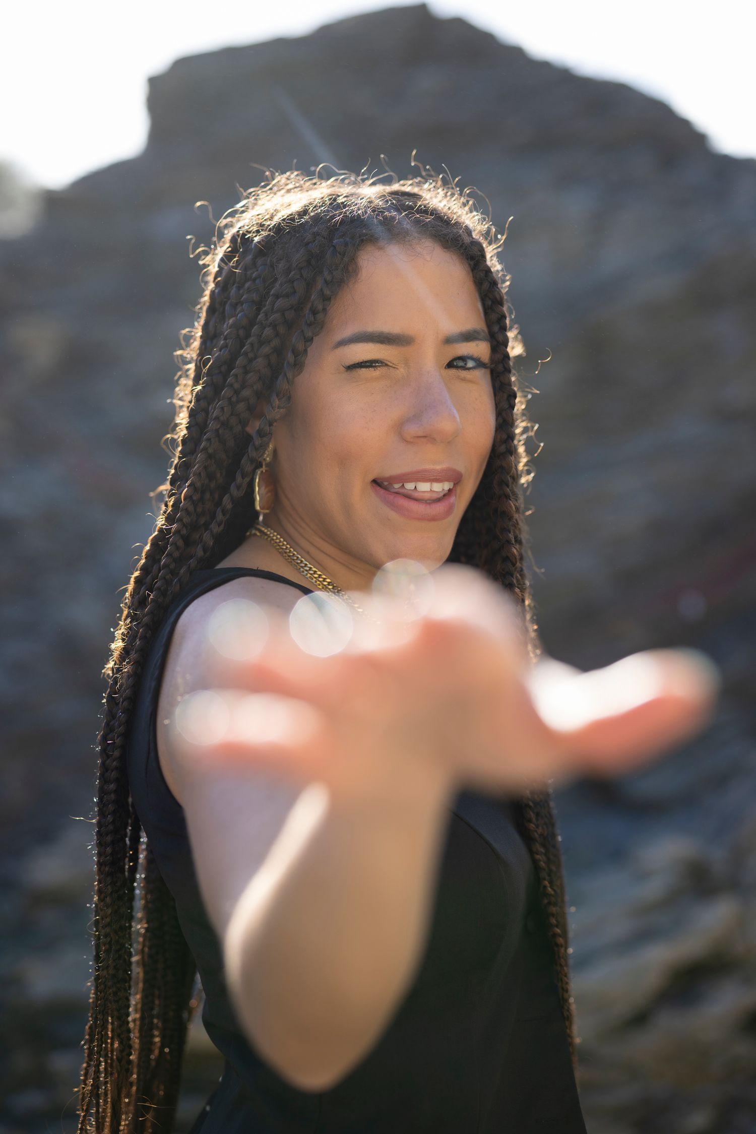 Portrait of a person with braided hair in sunlight reaching toward camera.