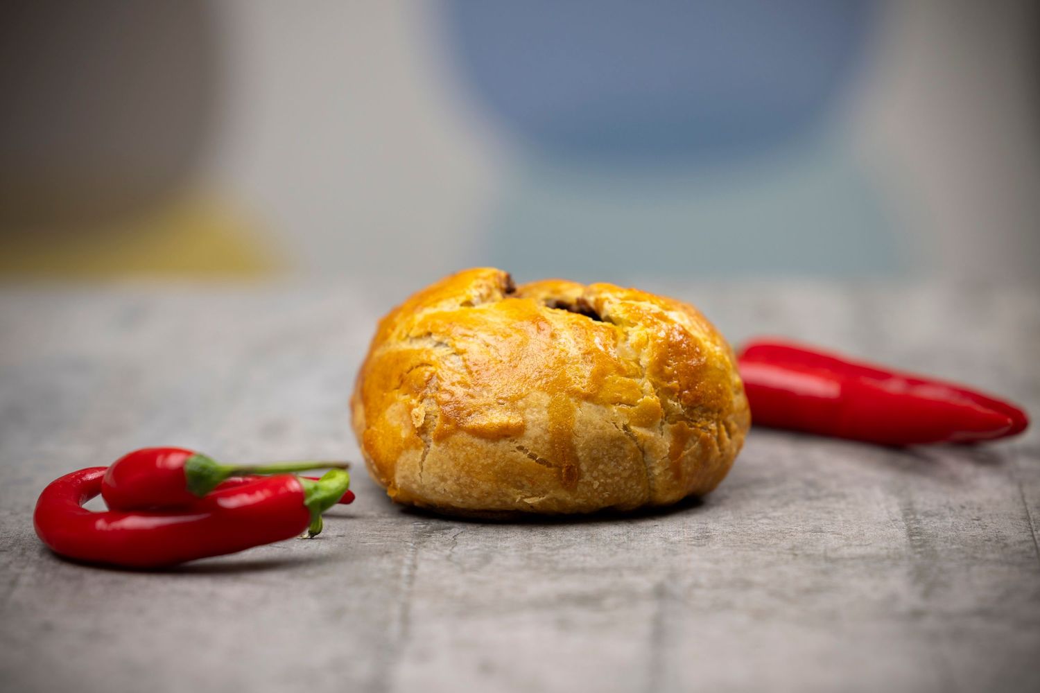 Golden baked rendang pie with red chili peppers on concrete surface.