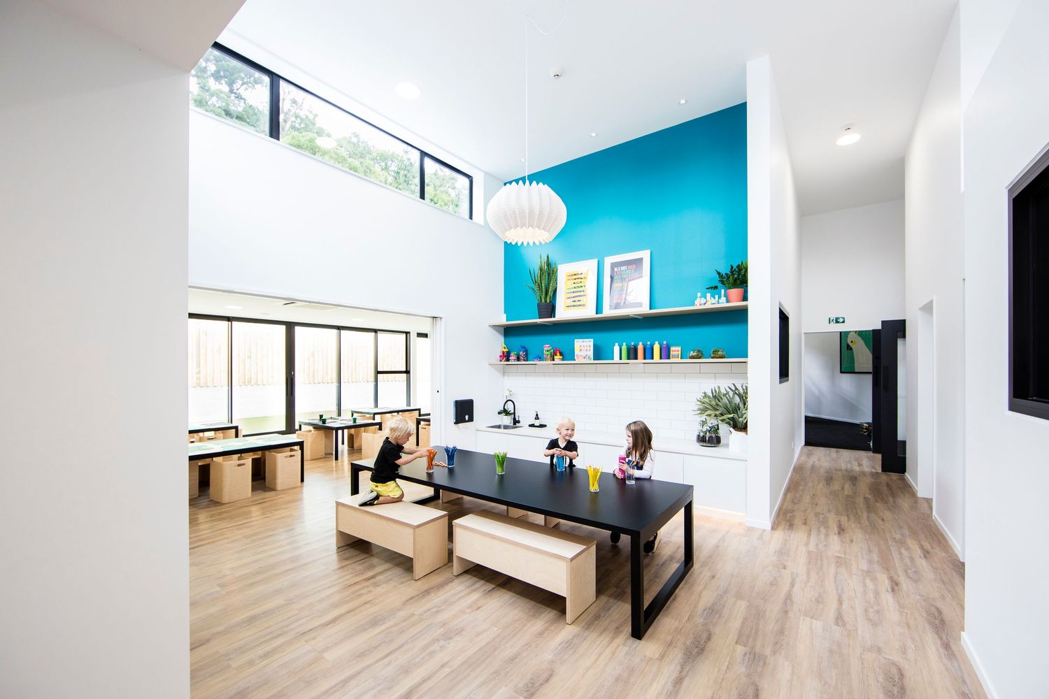 Contemporary office space with black dining table, wooden benches, and bright blue feature wall.