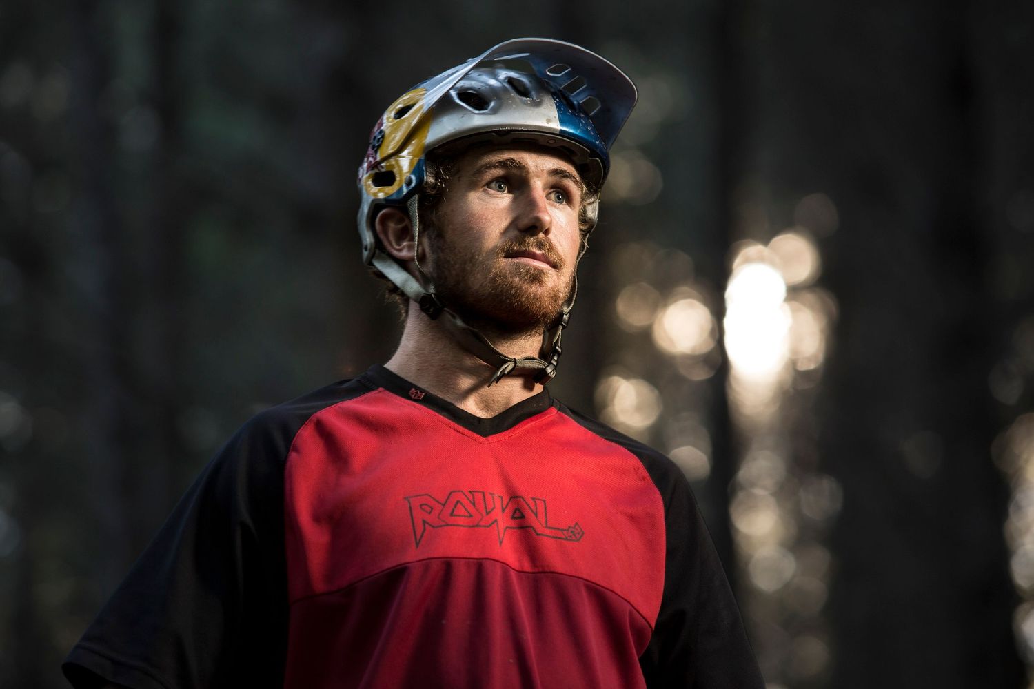 Mountain biker in red jersey riding through dark forest trail.