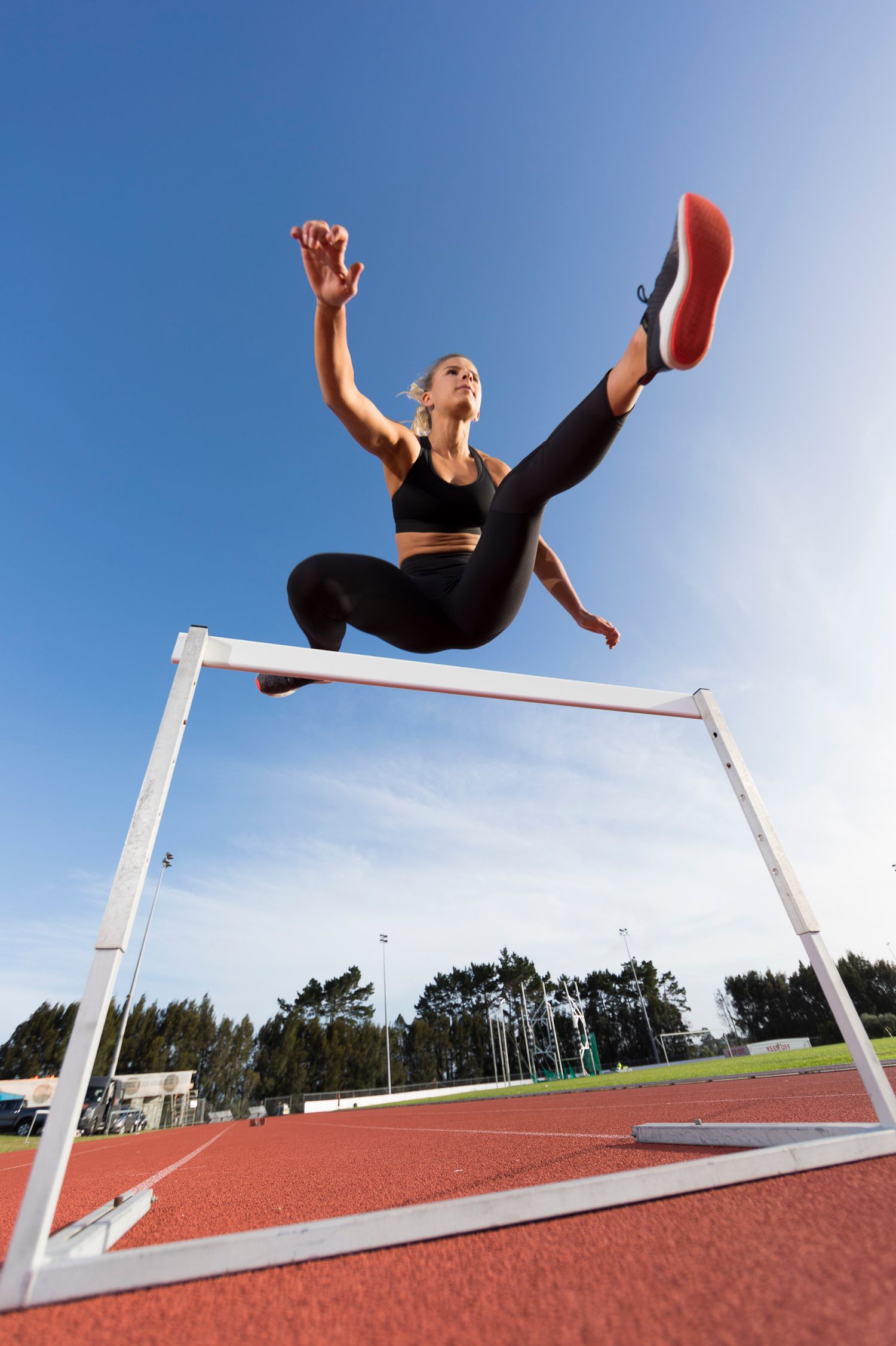 An athlete leaps gracefully over a high jump bar against a bright blue sky.